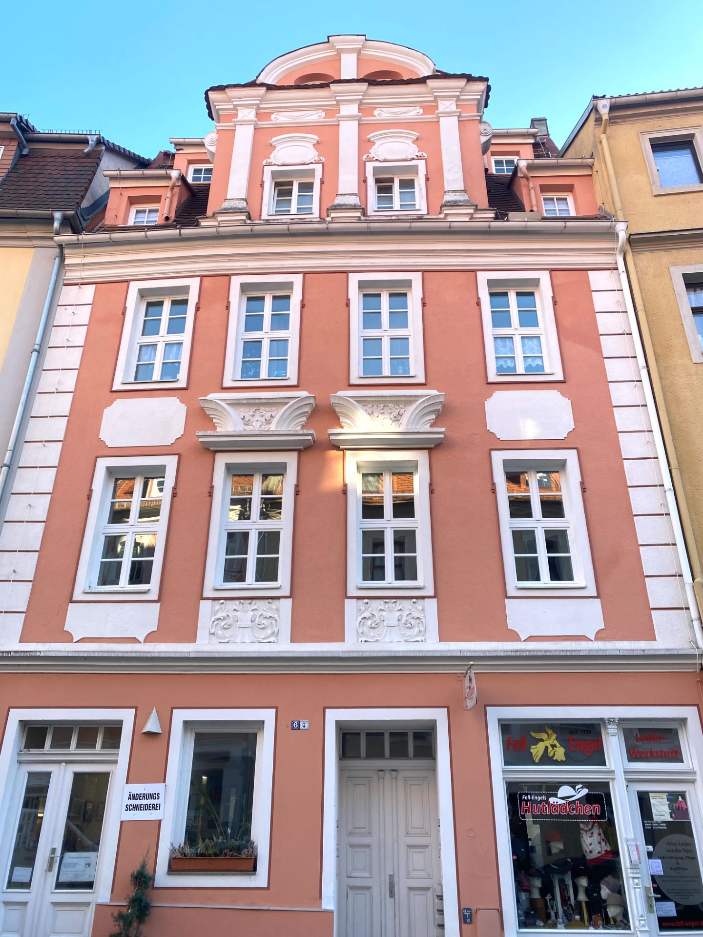 Mehrstöckiges orangefarbenes Wohnhaus mit weißem Stuck, großen Fenstern und Geschäften im Erdgeschoss.