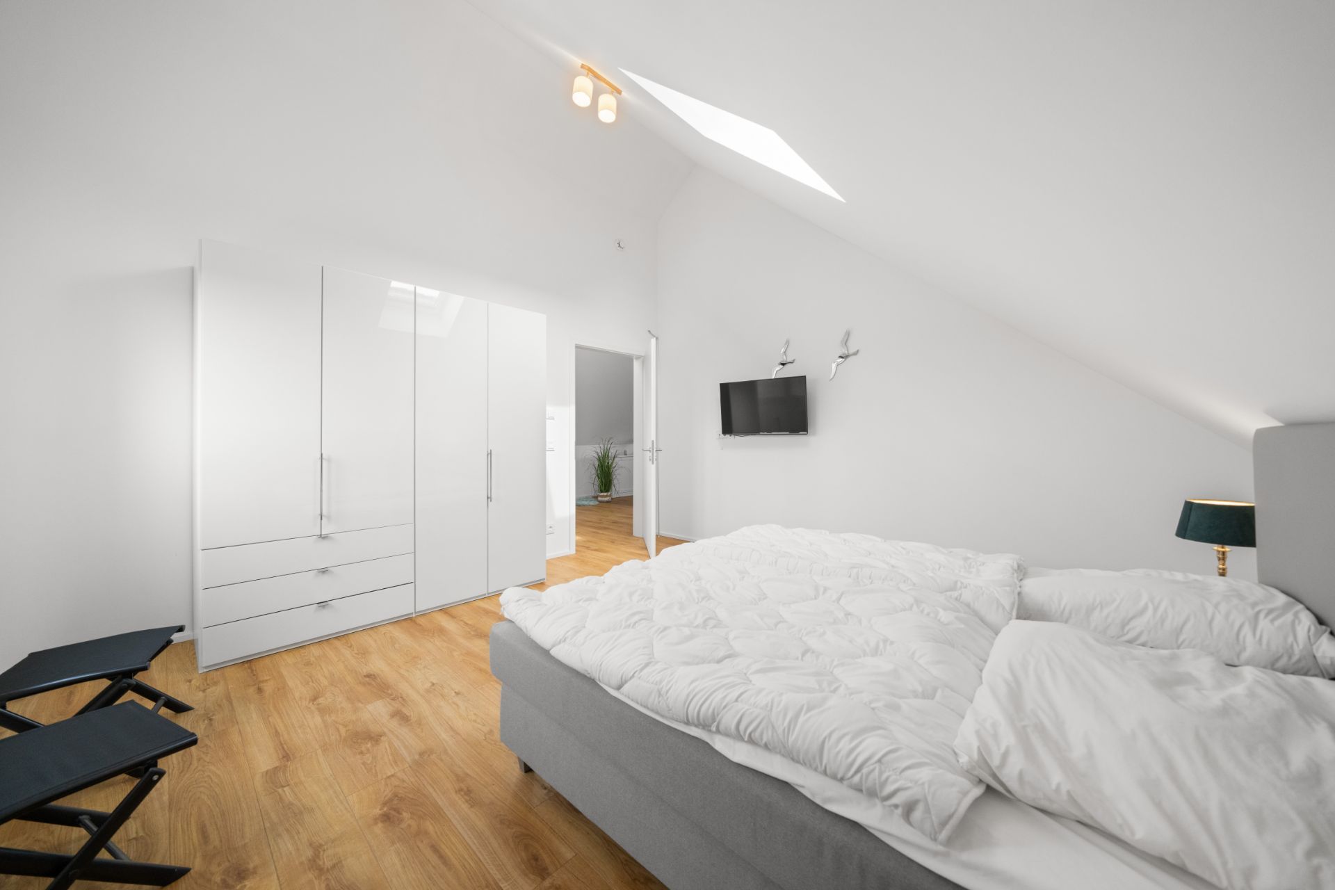 Helles Schlafzimmer mit Doppelbett, Kleiderschrank, Fernseher und Dachfenster.
