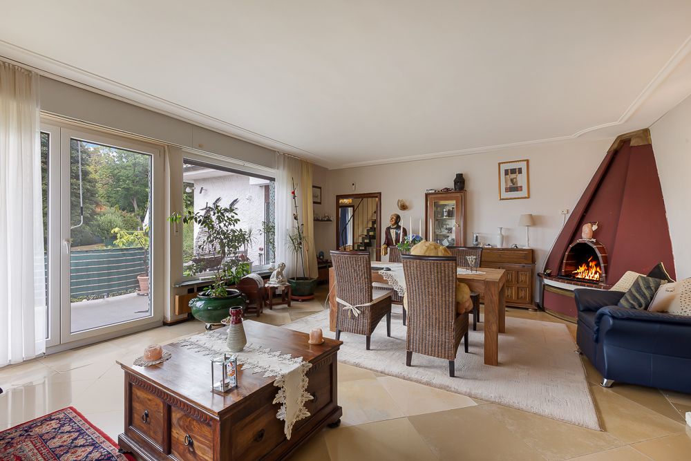 Wohnzimmer mit Esstisch, Kamin, großen Fenstern und Zugang zur Terrasse.