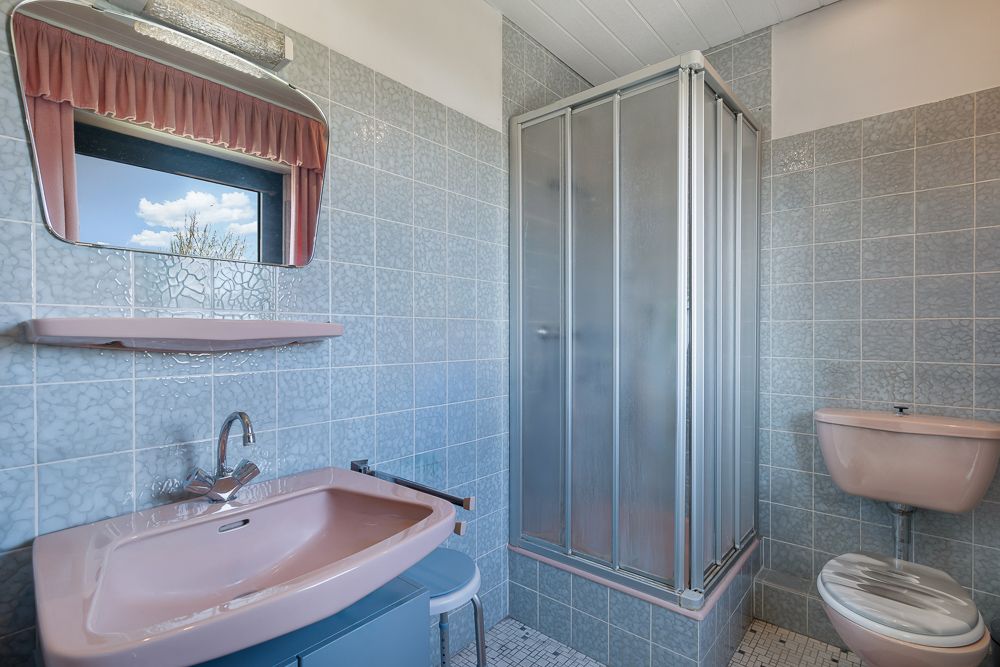 Badezimmer mit rosa Waschbecken, Dusche, Toilette und Spiegel mit Fenster.