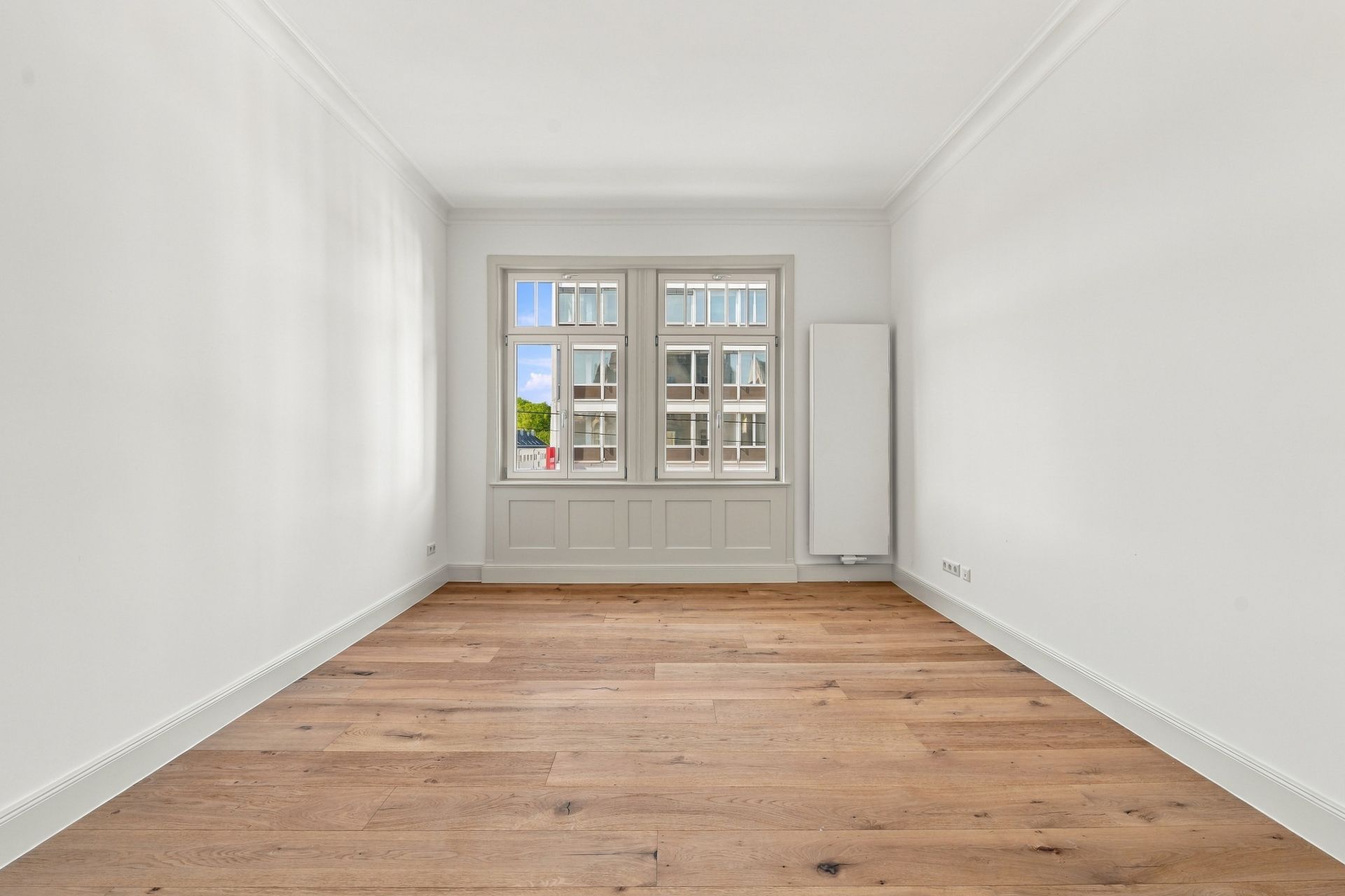 Leerer Raum mit Holzboden, weißem Wänden und drei Fenstern, Blick nach draußen.