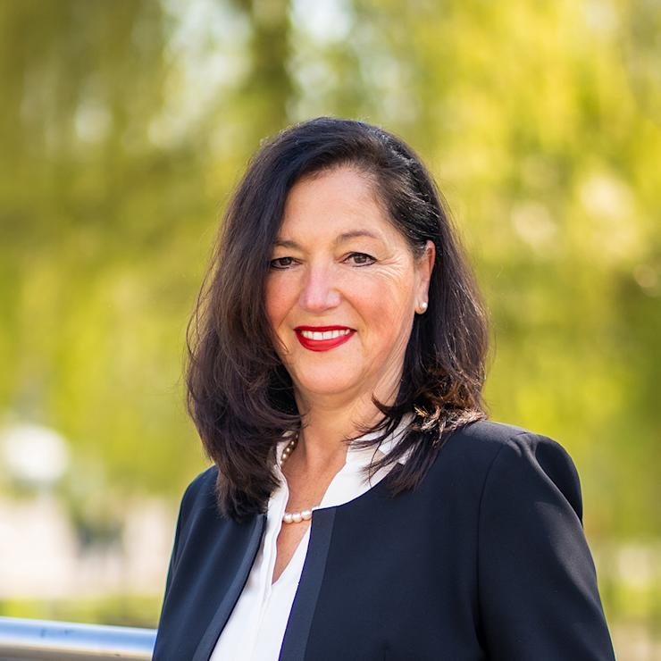 Frau mit dunklen Haaren und dunklem Blazer steht an einem Geländer im Freien.