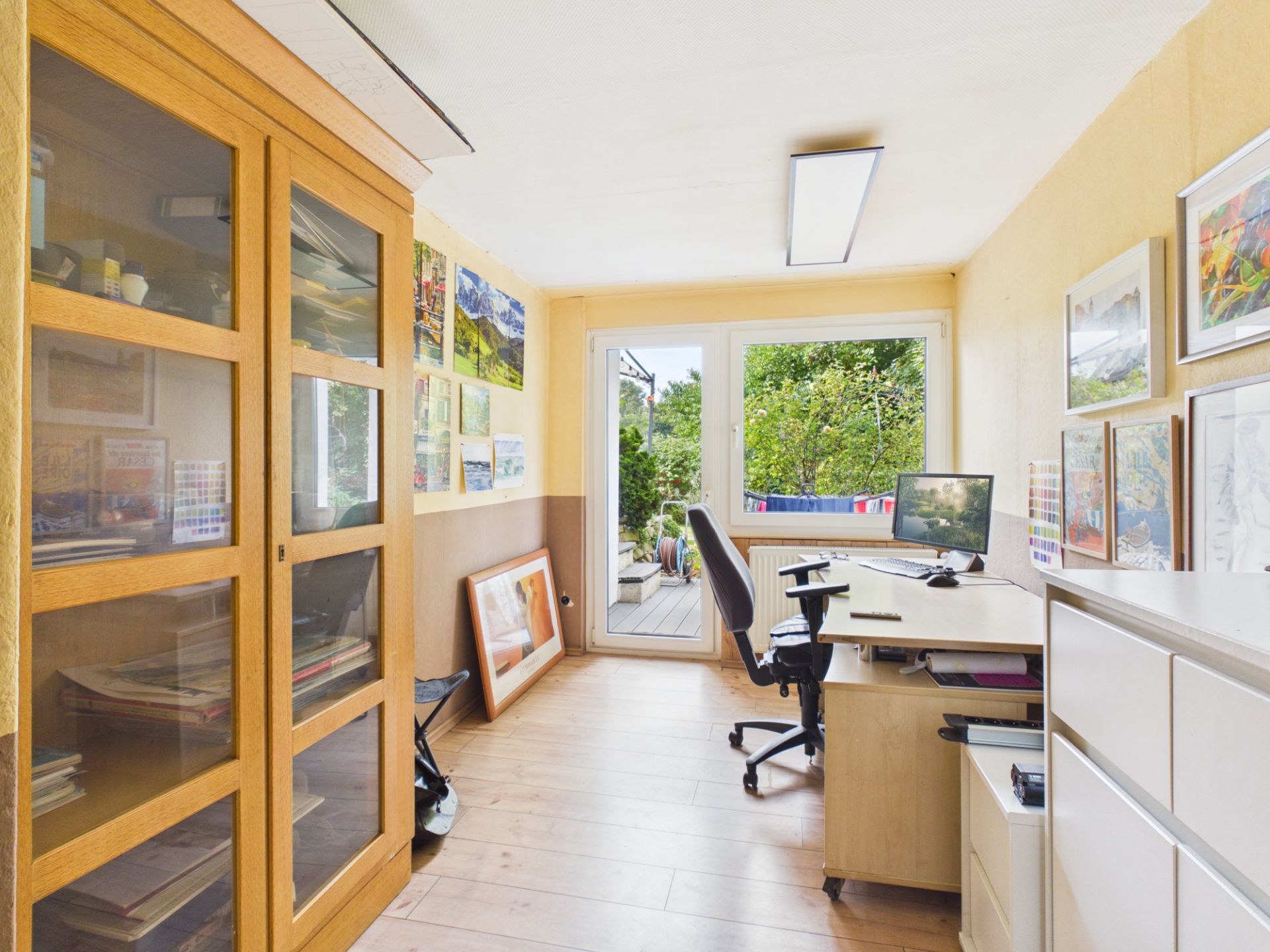 Helles Arbeitszimmer mit Schreibtisch, Stuhl, Regalen und Glastür zum Garten.