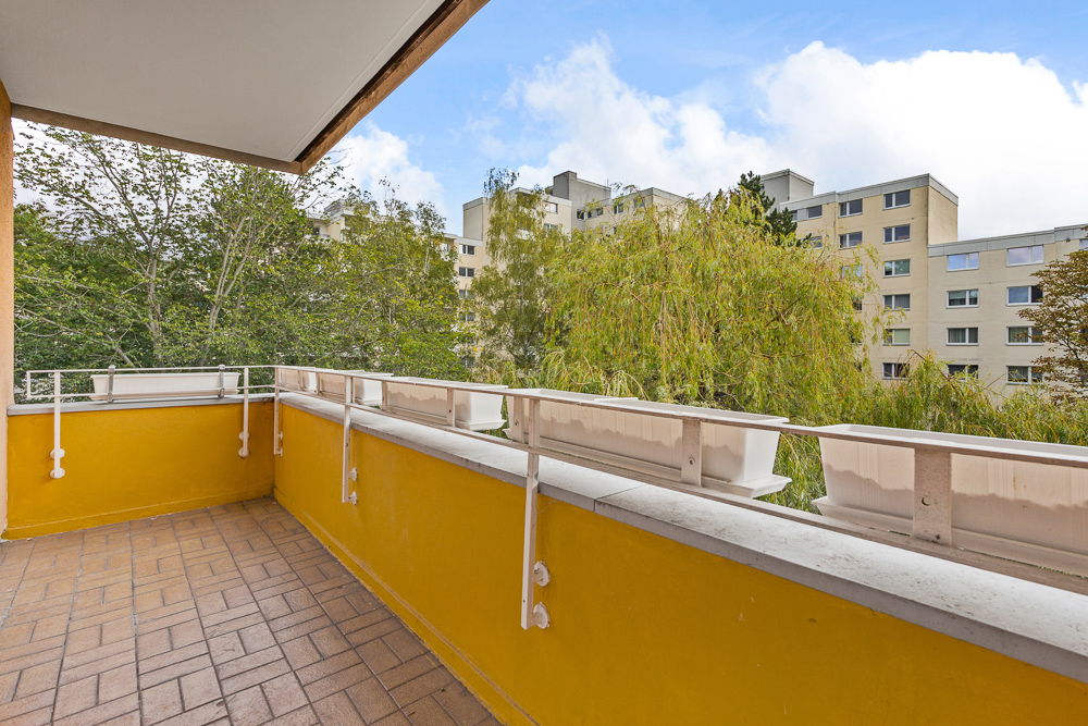 Balkon mit gelbem Geländer und Blick auf Bäume sowie benachbarte Wohngebäude.