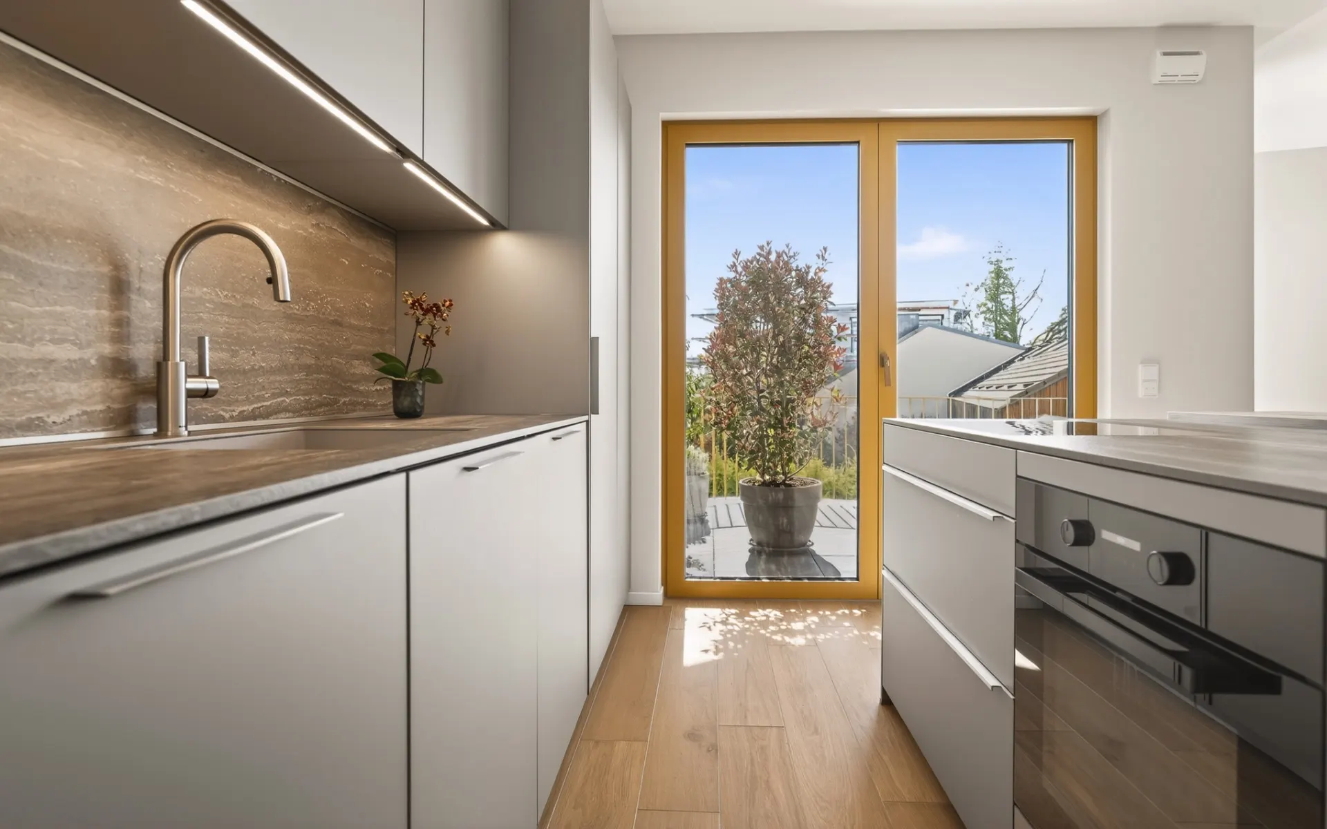 Moderne Küche mit Holzarbeitsplatte, integriertem Ofen und Blick auf Terrasse mit Pflanze.