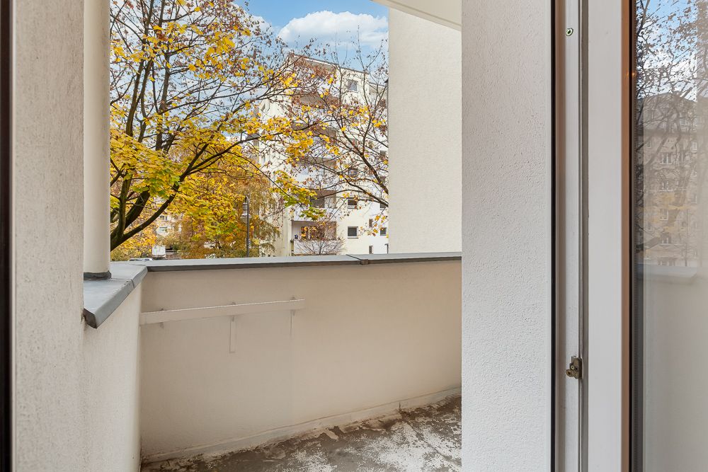 Kleiner Balkon mit Blick auf Bäume und Wohngebäude, begrenzt von weißen Wänden.