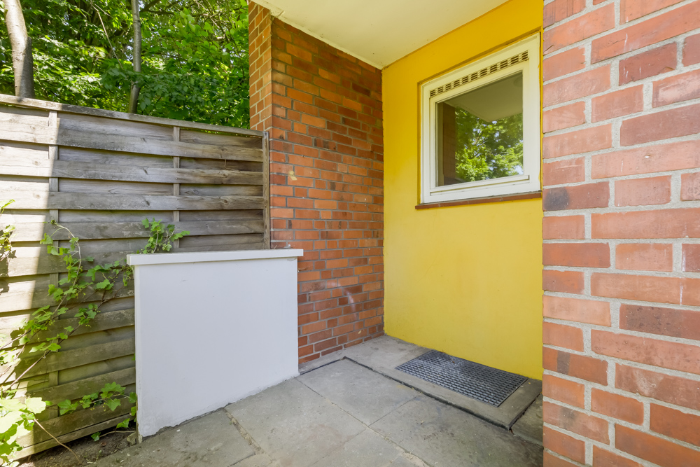 Kleine Hausecke mit gelber Wand, Fenster, Holzzaun und Pflastersteinen.