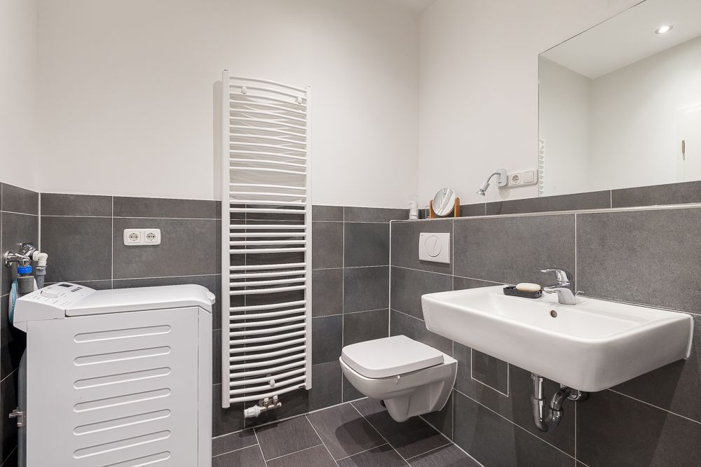 Modernes Bad mit Waschmaschine, Wandtoilette, Waschbecken und Handtuchheizkörper.