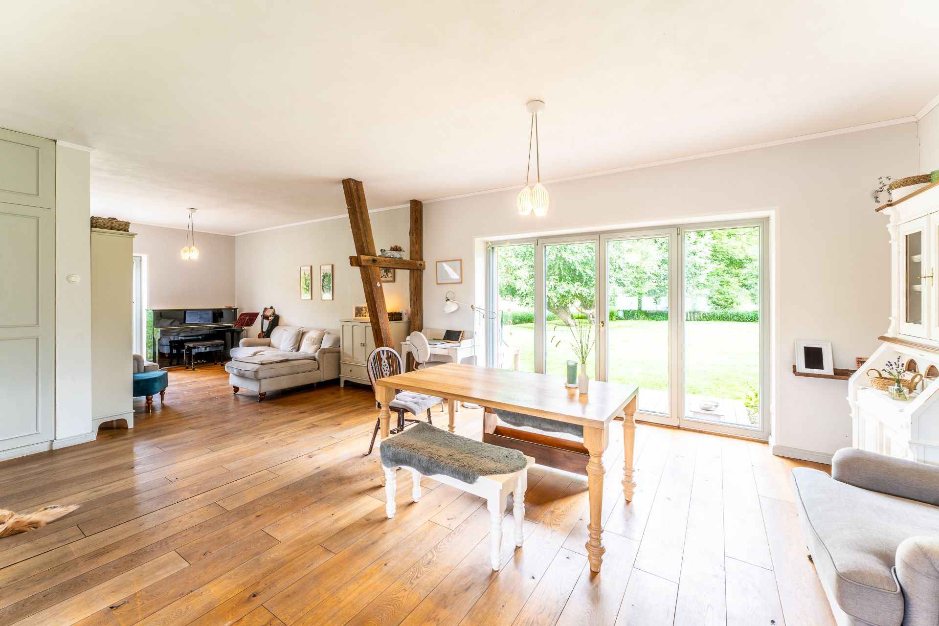 Helles Wohnzimmer mit Holzboden, Esstisch, Sofa und großen Fenstern zum Garten.