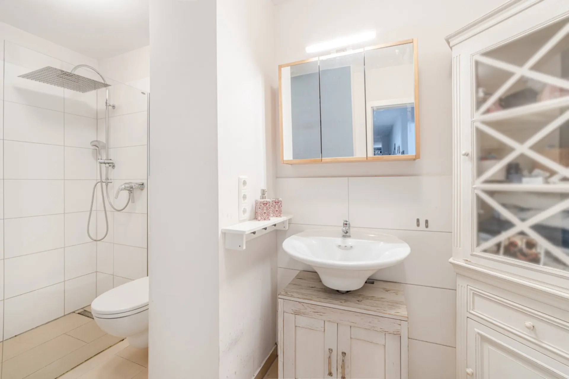 Helles Badezimmer mit Dusche, Waschbecken, Spiegelschrank und weißem Schrank.