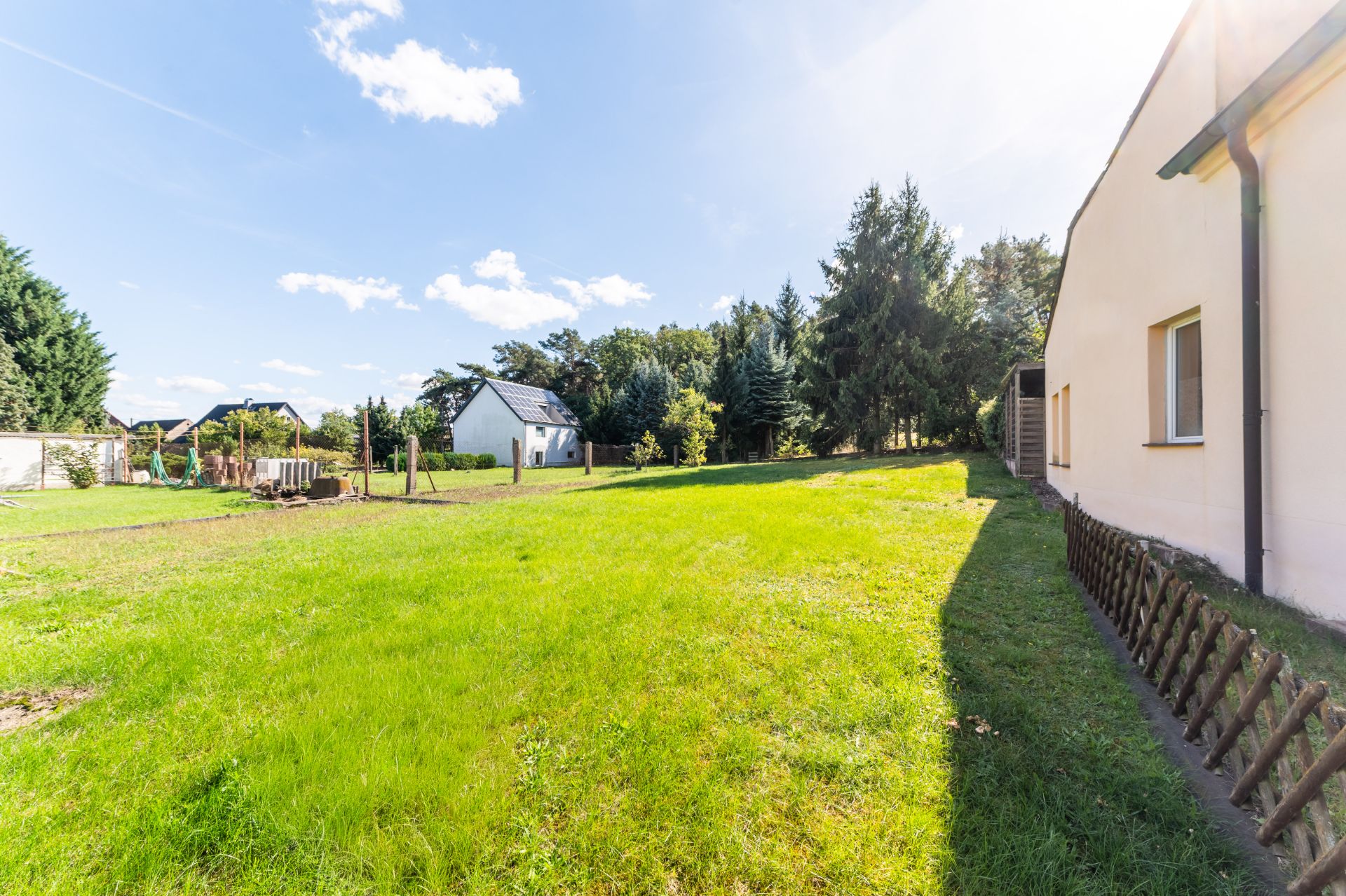 Großer grüner Garten mit Rasen, Bäumen und einem Haus am rechten Bildrand.