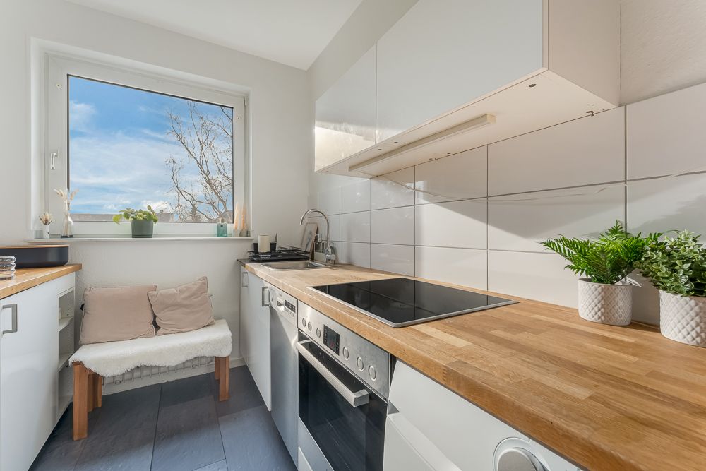 Helle, moderne Küche mit Holzarbeitsplatte, Herd, Pflanzen und Sitzbank am Fenster.