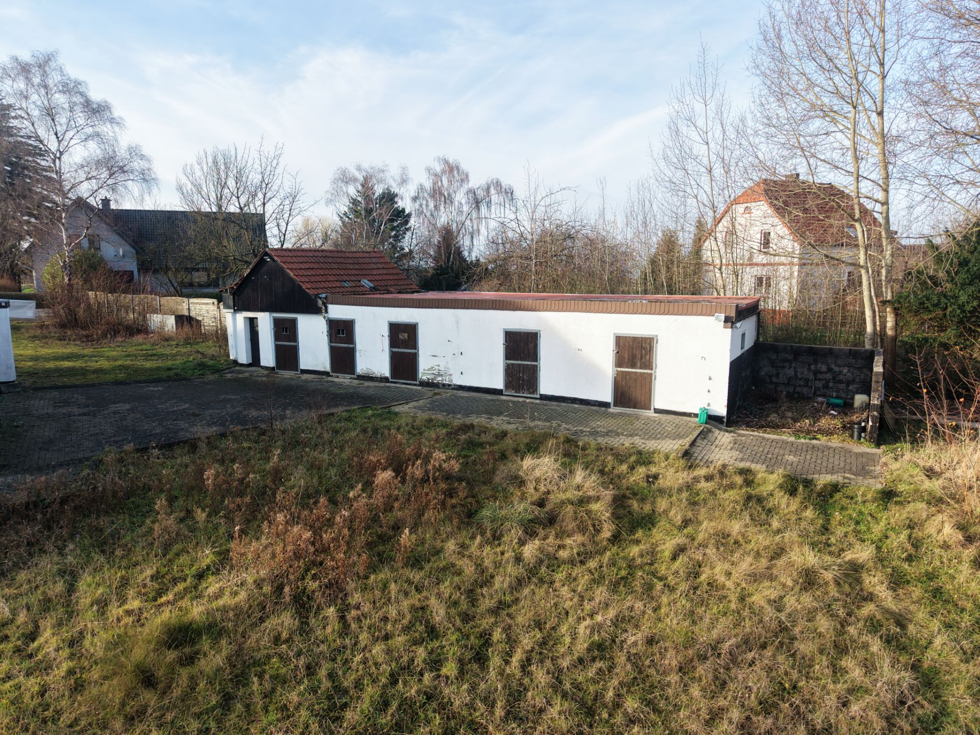 Langes, einstöckiges Nebengebäude mit mehreren Holztüren im Gartenbereich.
