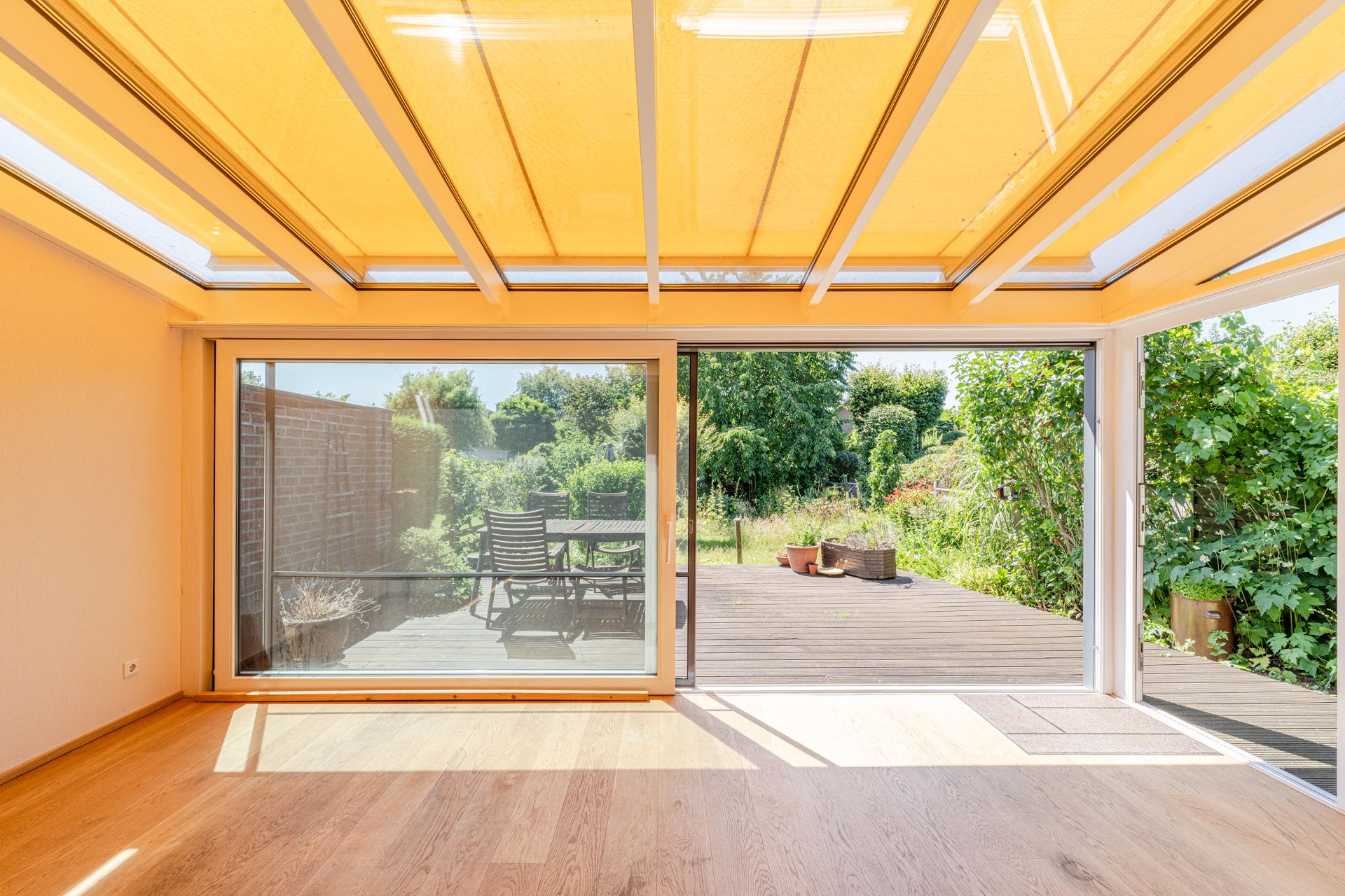 Heller Wintergarten mit Holzfußboden, Blick auf Terrasse mit Gartenmöbeln und Garten.