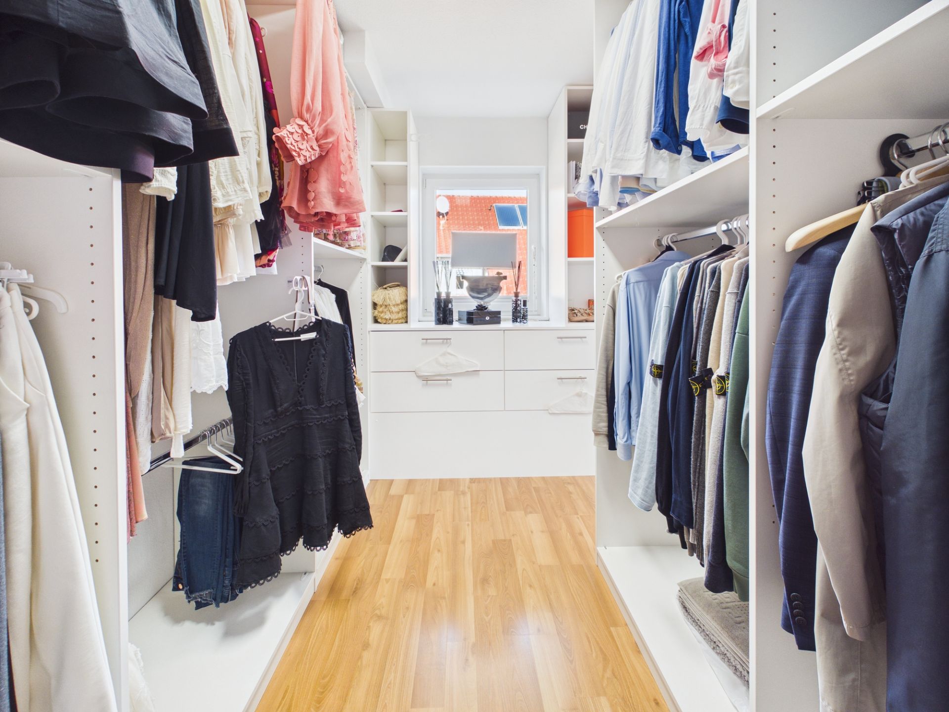 Geräumiger begehbarer Kleiderschrank mit Kleidung, Regalen und Spiegel auf Holzfußboden.