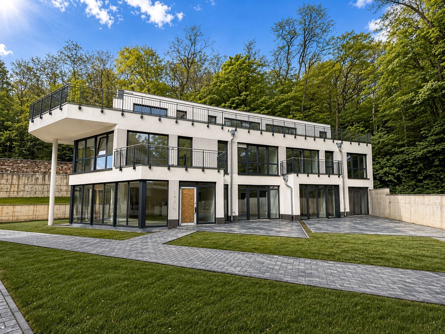 Modernes, zweistöckiges Wohnhaus mit großen Fenstern und mehreren Balkonen, umgeben von Rasen und Wald.