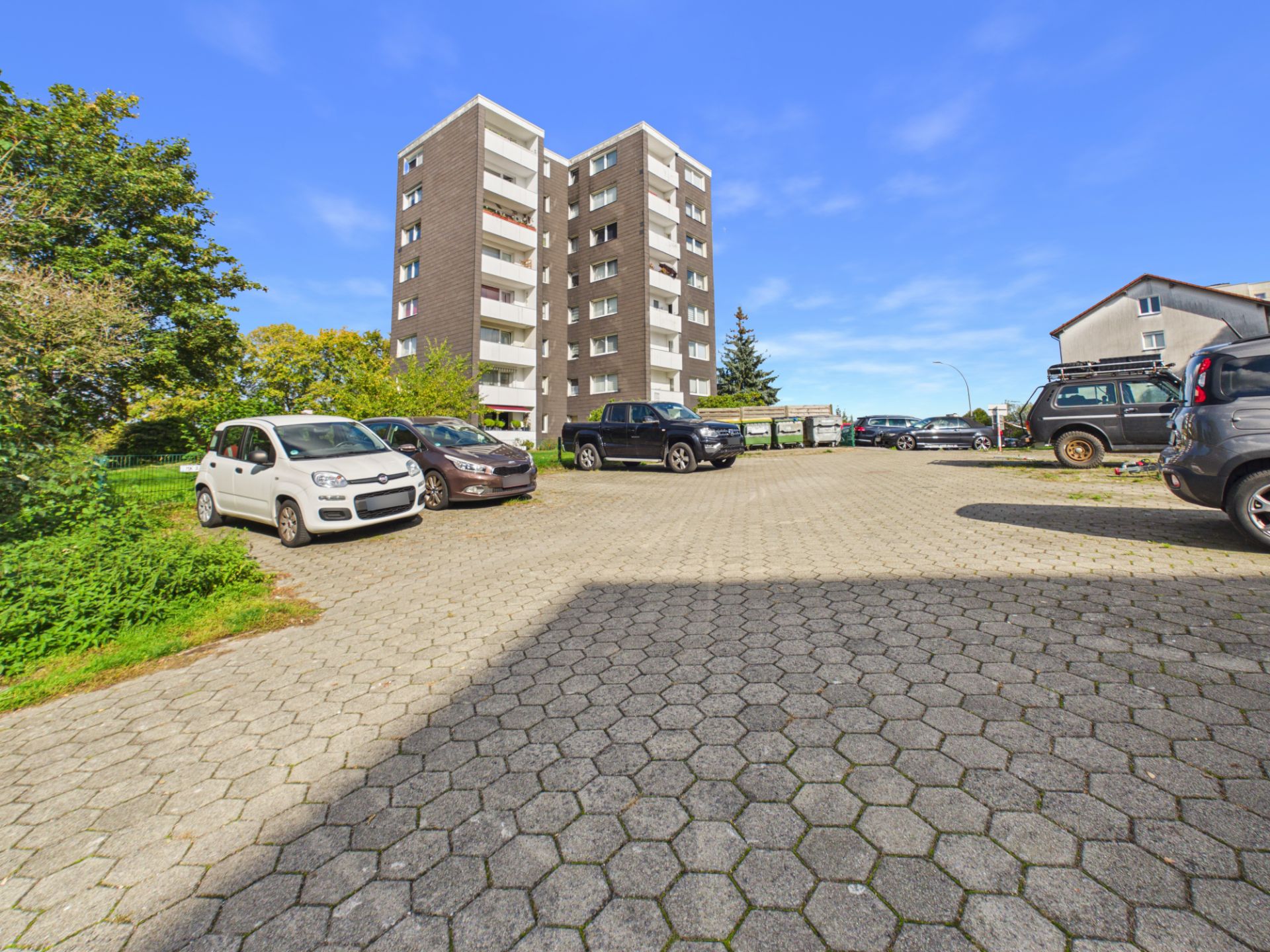 Mehrstöckiges Wohngebäude mit gepflastertem Parkplatz und mehreren geparkten Autos.