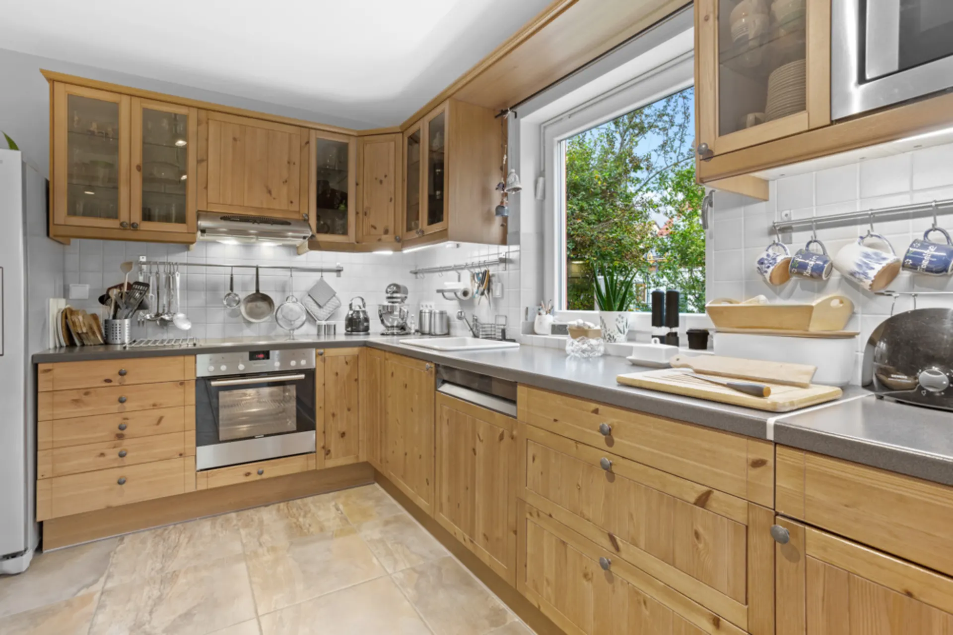 Moderne Küche mit Holzmöbeln, Herd, Spüle, großem Fenster und Küchenutensilien auf der Arbeitsfläche.