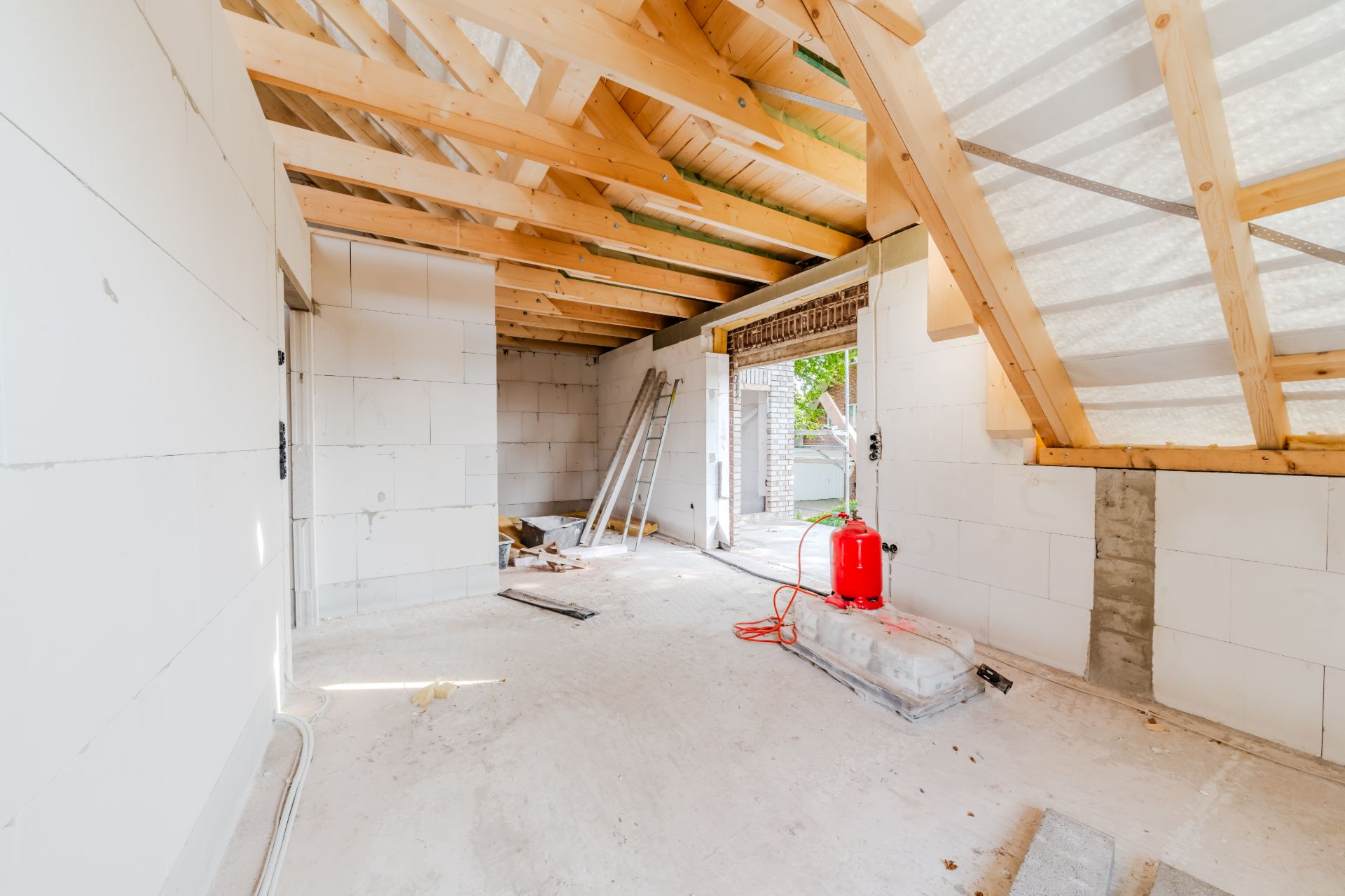 Innenraum eines Hauses im Rohbau mit sichtbarem Dachstuhl, Leiter und Baumaterialien.