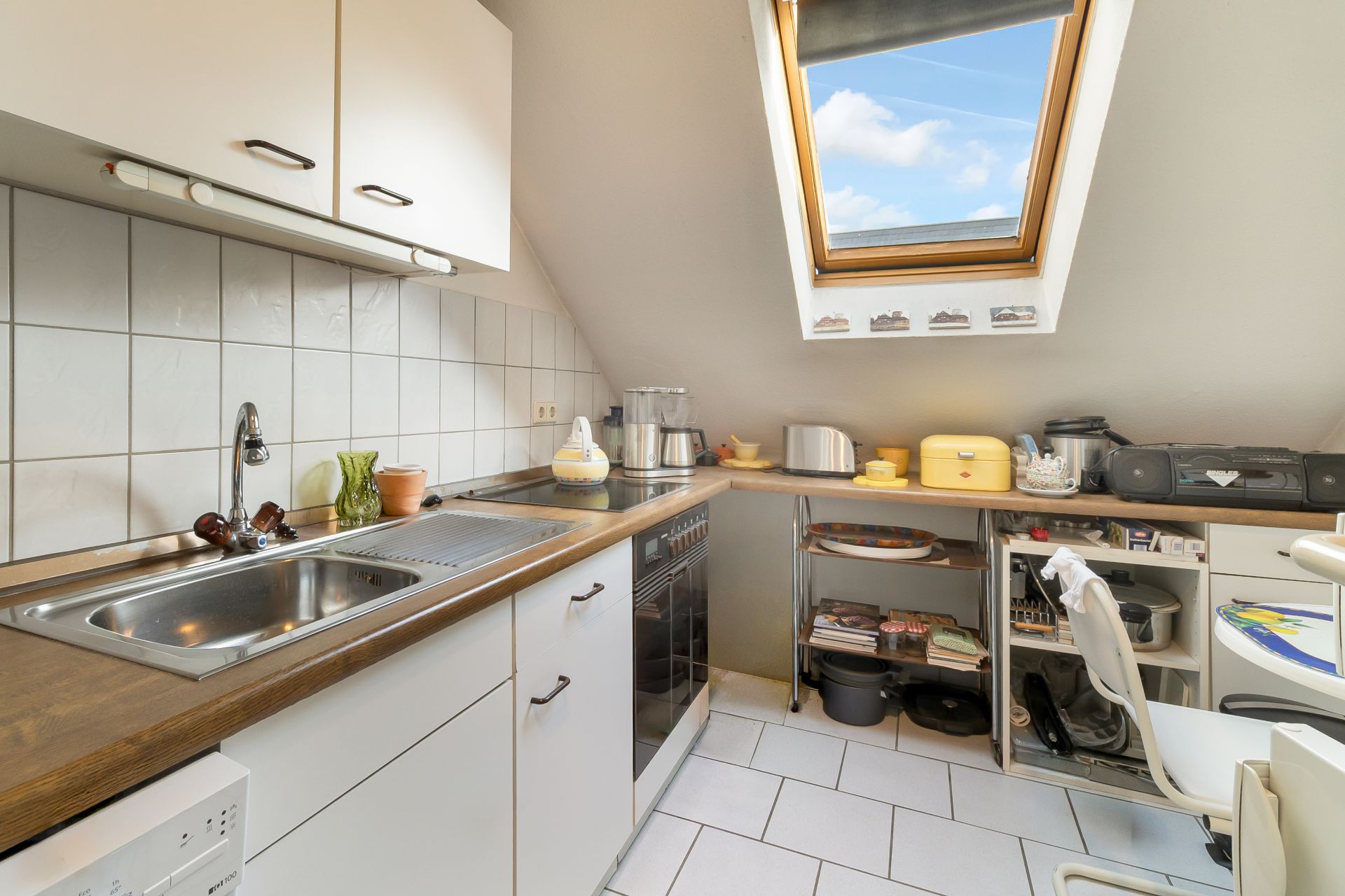 Helle Küche mit Dachfenster, weißem Schrank, Spüle, Herd und Küchenutensilien.
