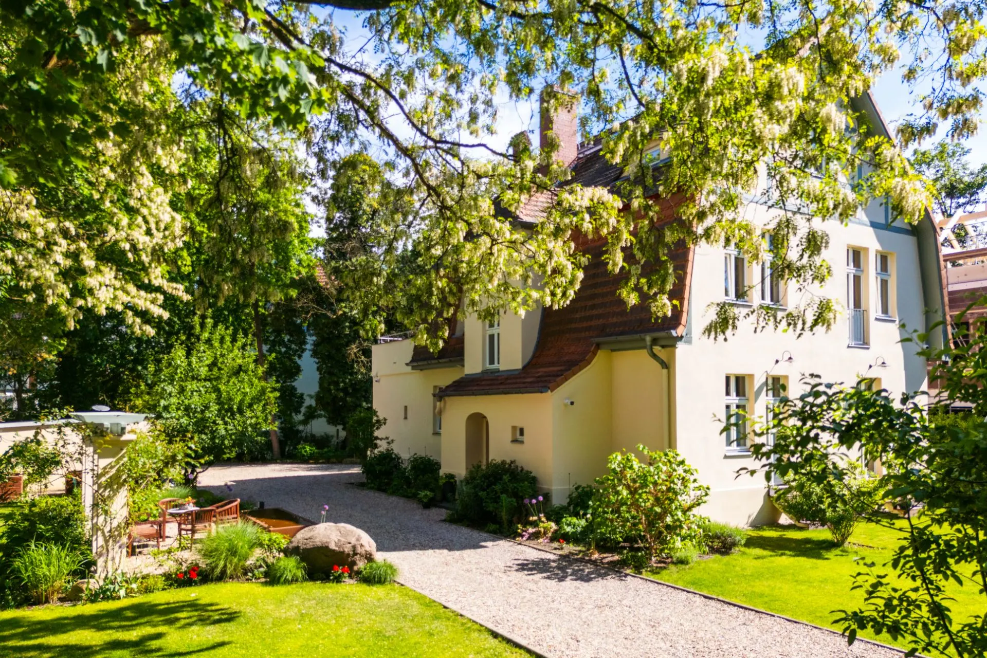 Helles Einfamilienhaus mit Garten, Kiesweg und Sitzbereich im Grünen.