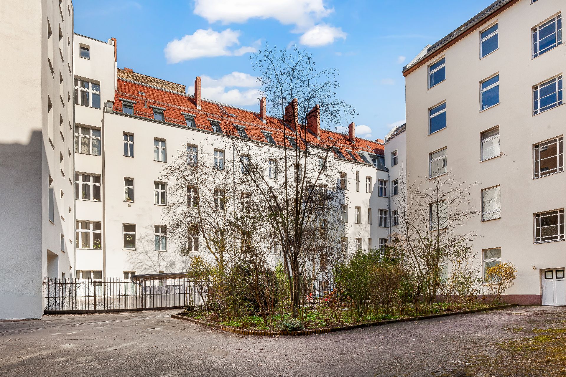 Innenhof mit umliegenden Wohngebäuden, Bäumen und Beeten, umgeben von weißen Fassaden.