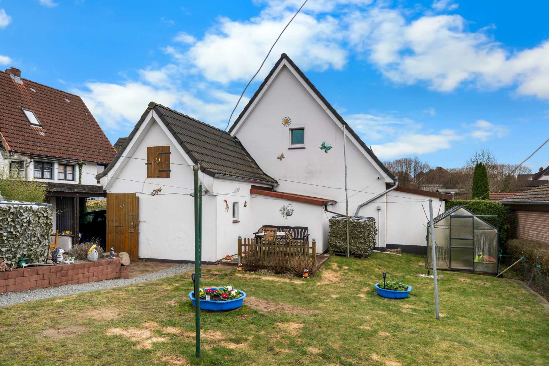 Hinterhof eines Wohnhauses mit Garten, Gartenmöbeln, Blumenbeet und Gewächshaus.