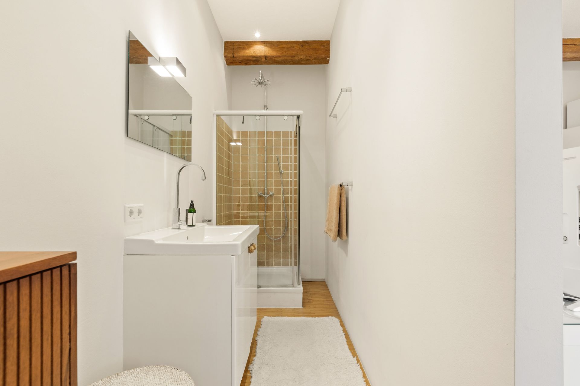 Modernes Badezimmer mit weißem Waschbecken, Spiegel und Duschkabine mit braunen Fliesen.