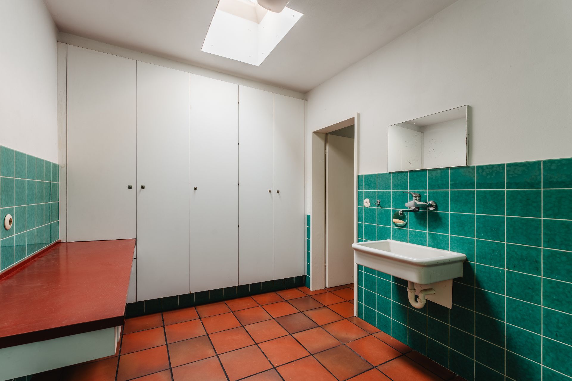 Raum mit roten Fliesen, grünen Wandfliesen, Waschbecken und weißen Einbauschränken.