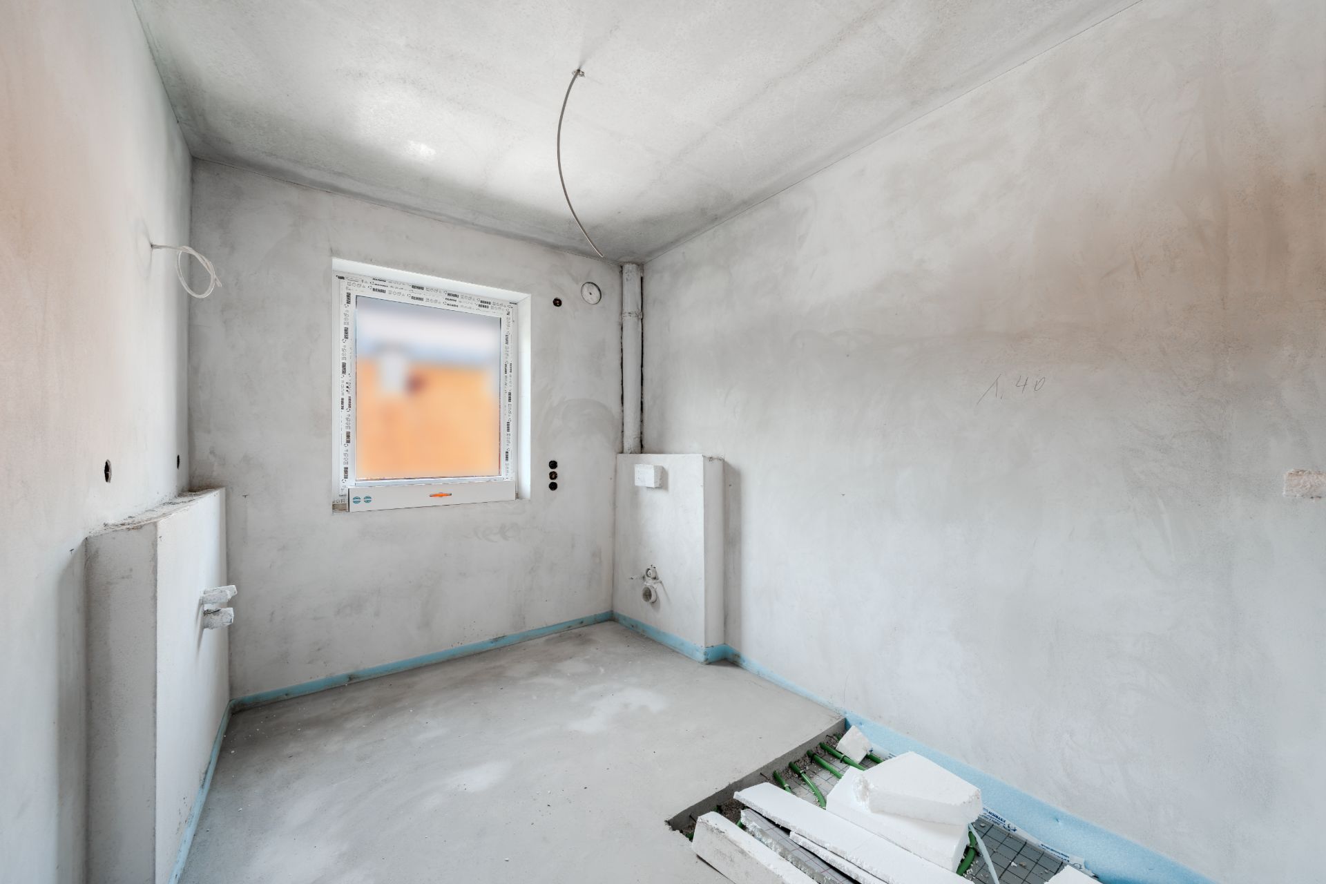 Unfertiger Raum mit grauen Wänden, Fenster und sichtbaren Installationen.