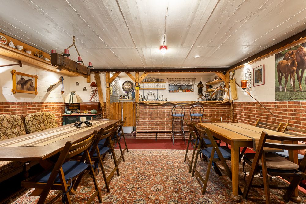 Gemütlicher Raum mit Holztischen, Stühlen, Theke aus Ziegeln und Teppich, dekoriert mit Pferdebildern.