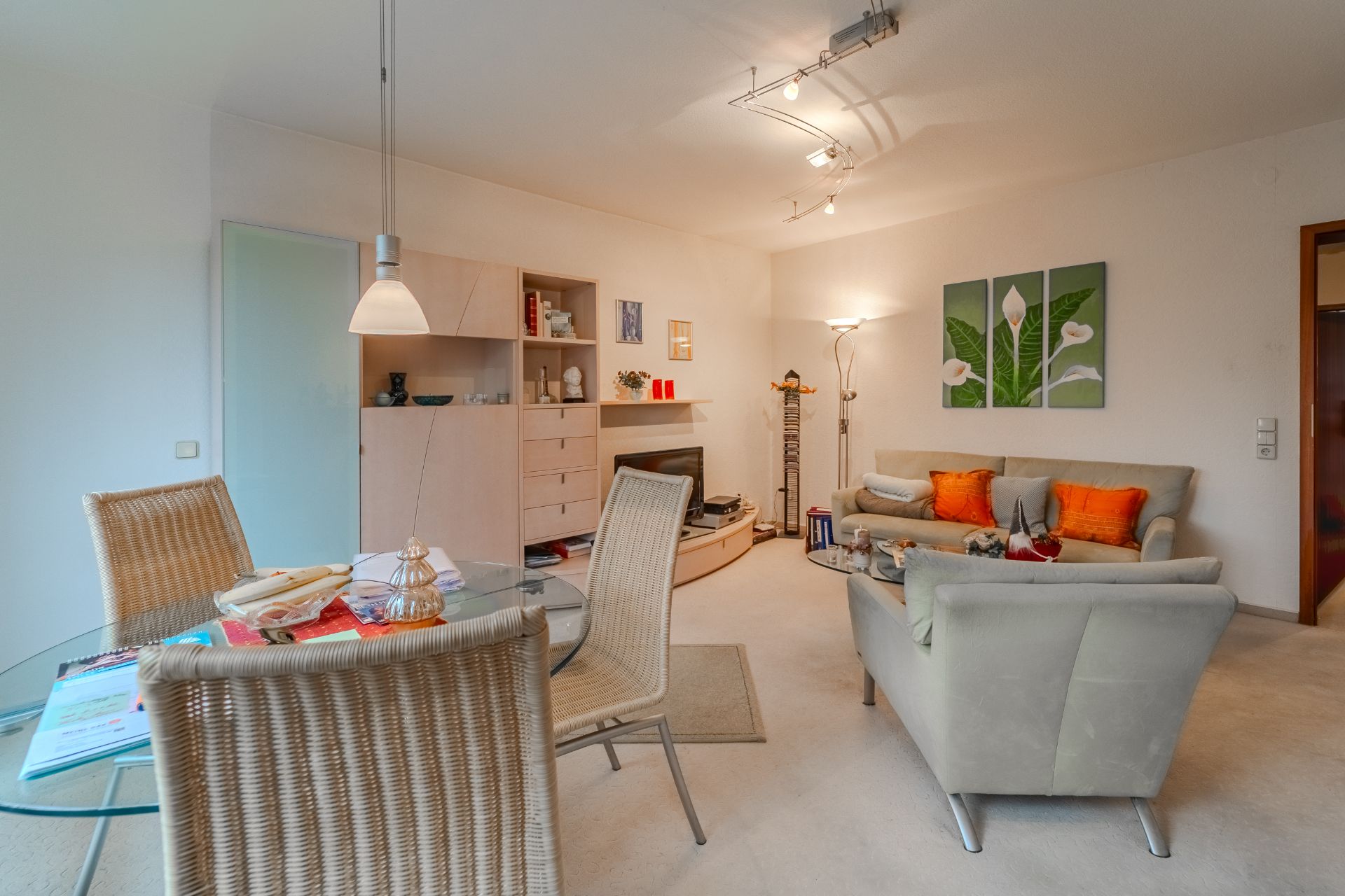 Helles Wohnzimmer mit Sitzecke, Esstisch, Regalen und Blumendekor an der Wand.