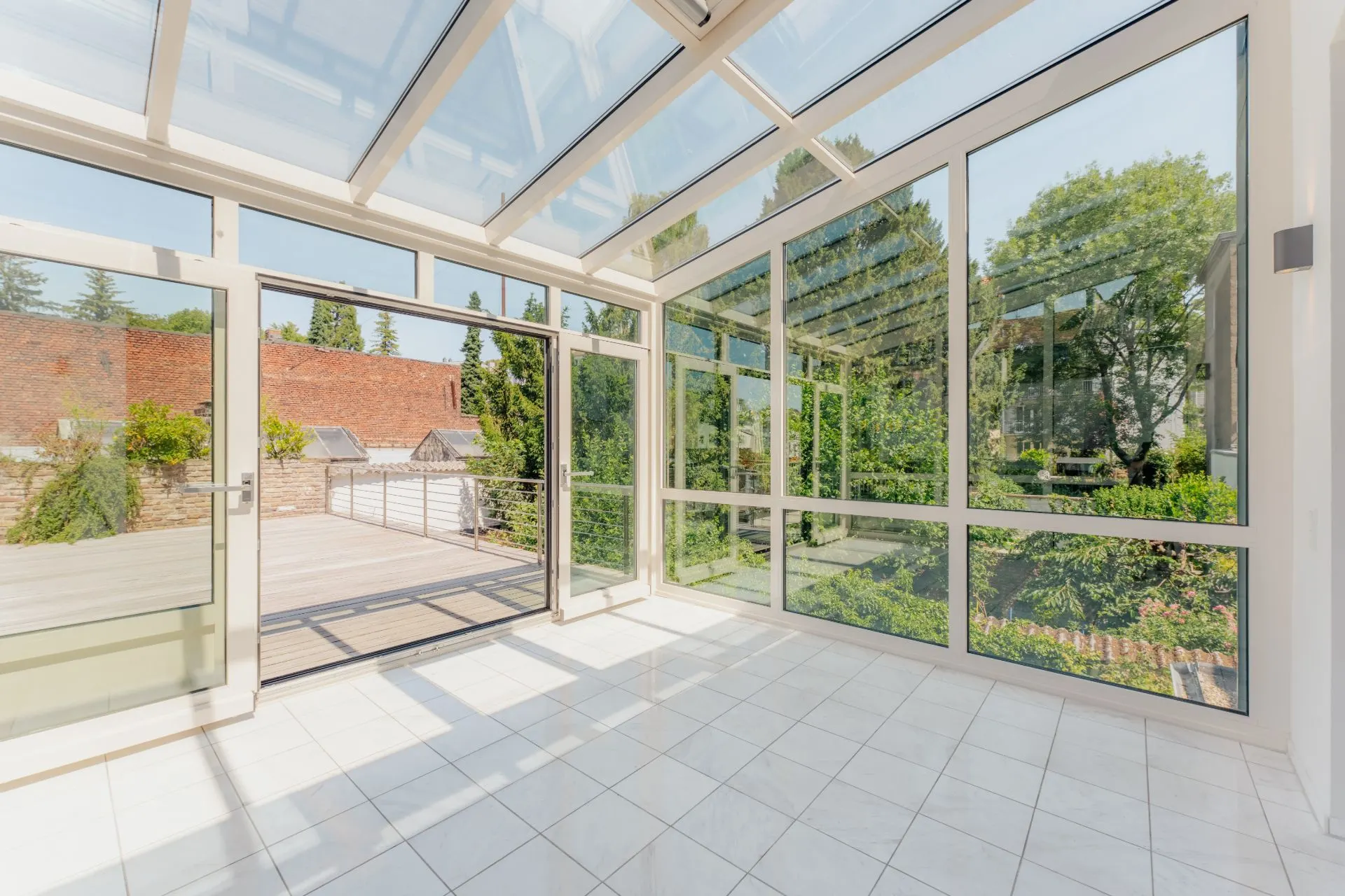 Heller Wintergarten mit Glasdach und großen Fenstern, Blick auf Terrasse und Garten.