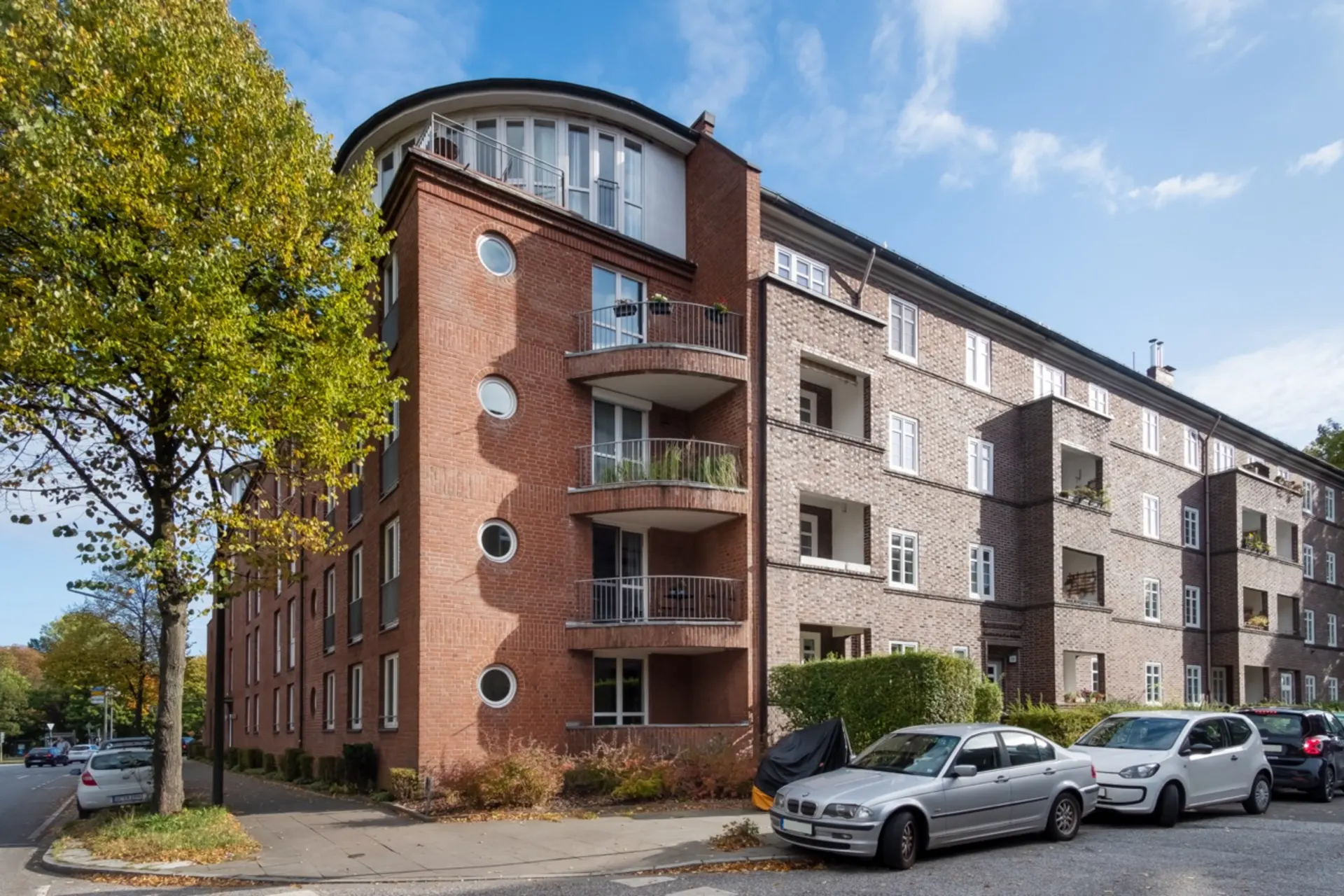 Mehrstöckiges Wohnhaus mit Balkonen und geparkten Autos davor.