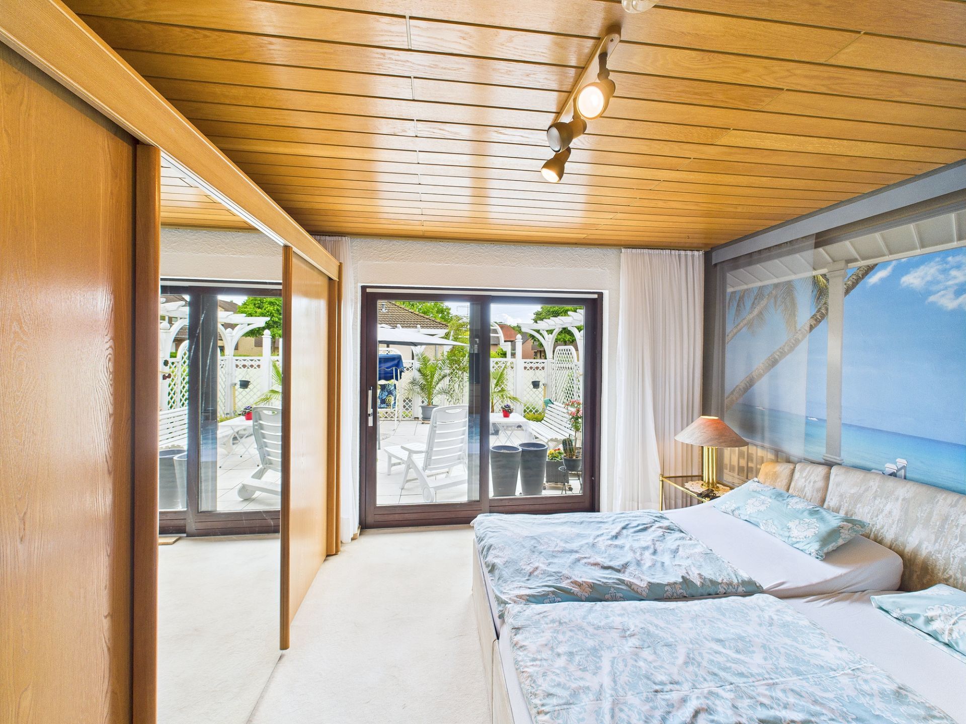 Helles Schlafzimmer mit zwei Betten, großer Glastür und Wandbild mit Strandmotiv.