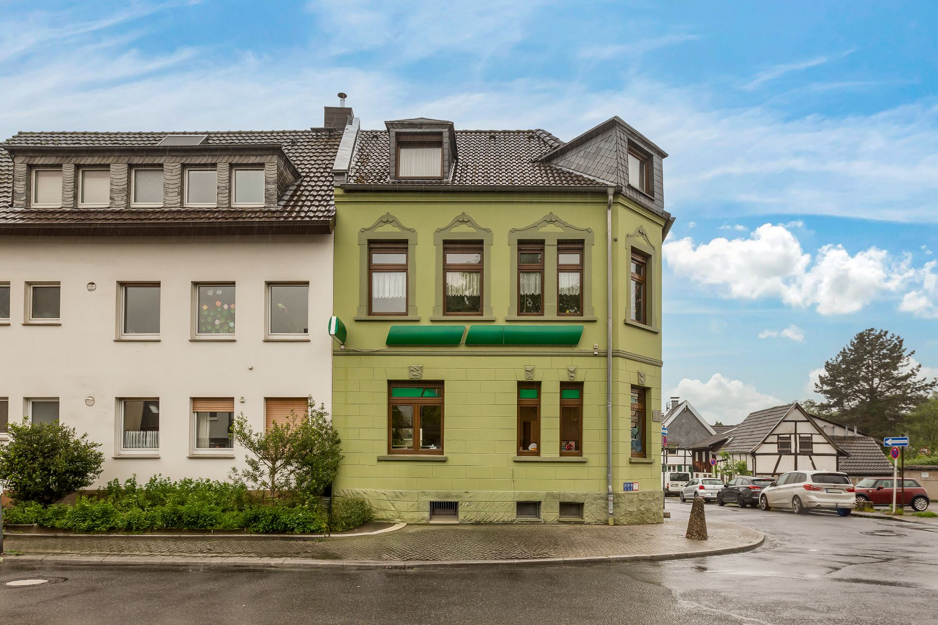 Eckhaus mit grünem Anstrich und mehreren Fenstern an einer Straße bei bewölktem Himmel.