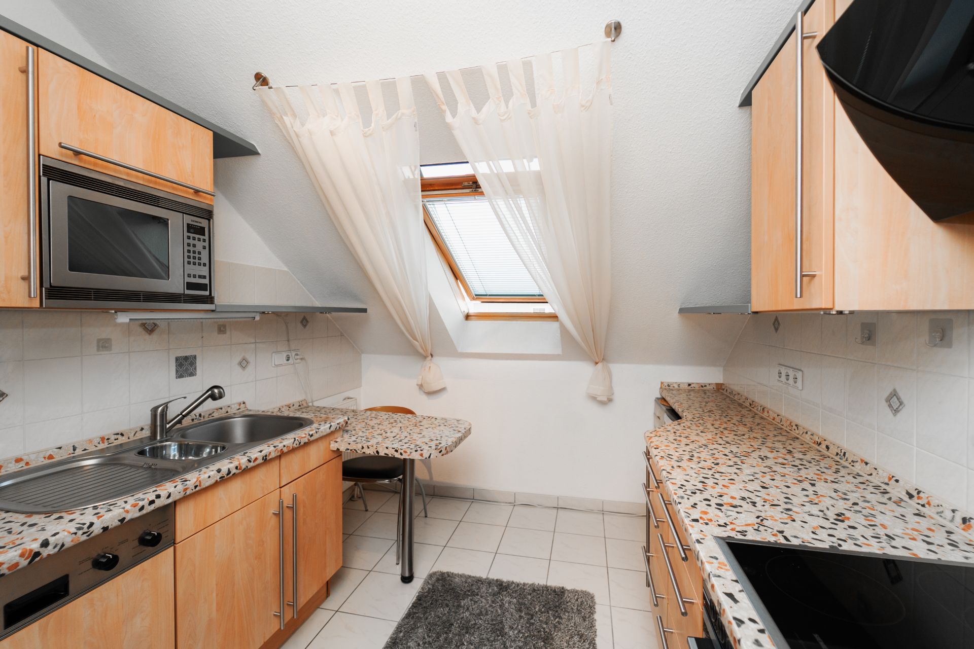 Kleine Küche mit Fenster, Spüle, Herd, Mikrowelle und Holzschränken.
