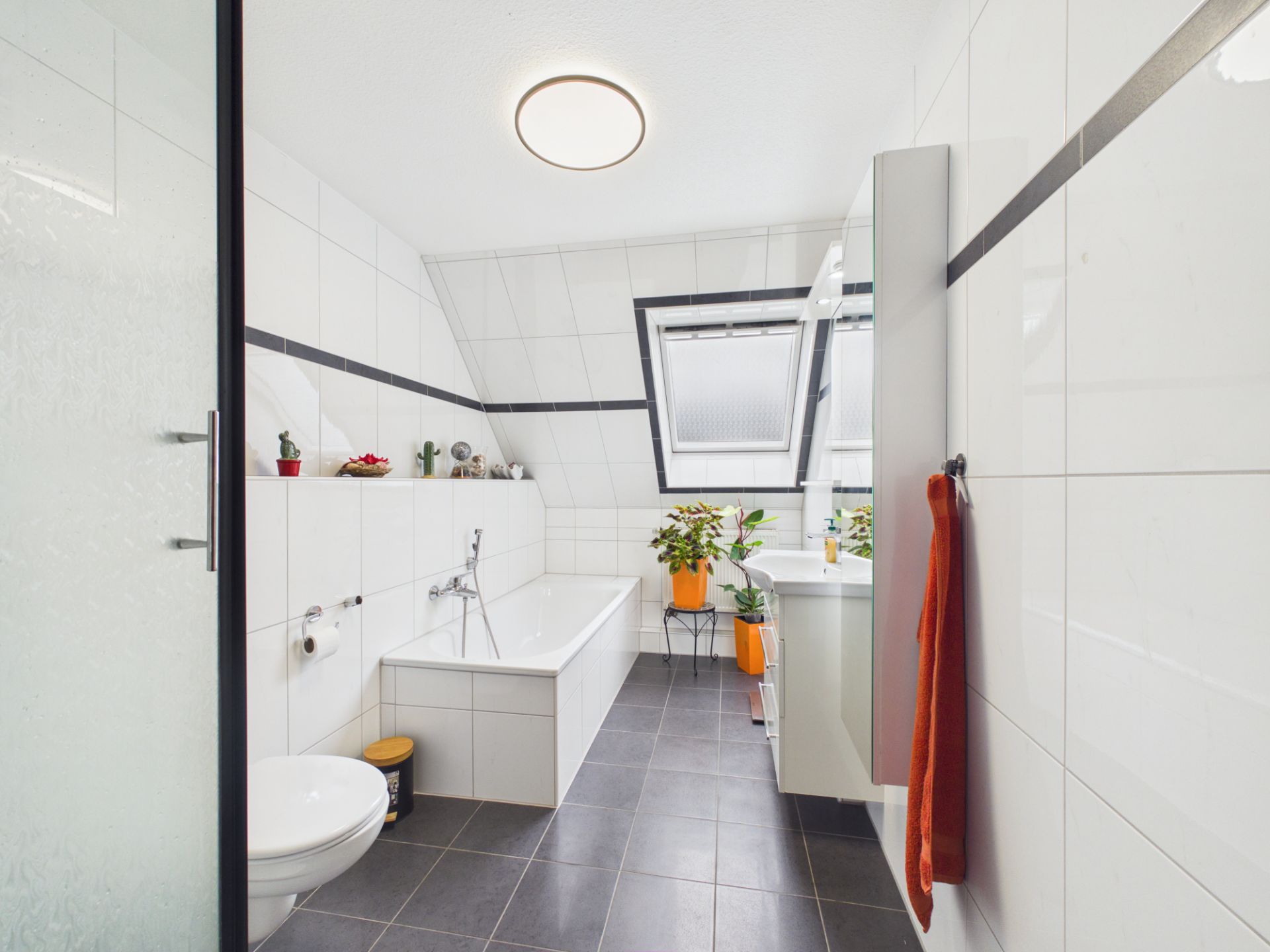 Modernes Badezimmer mit Badewanne, WC, Waschbecken und Pflanzen am Fenster.
