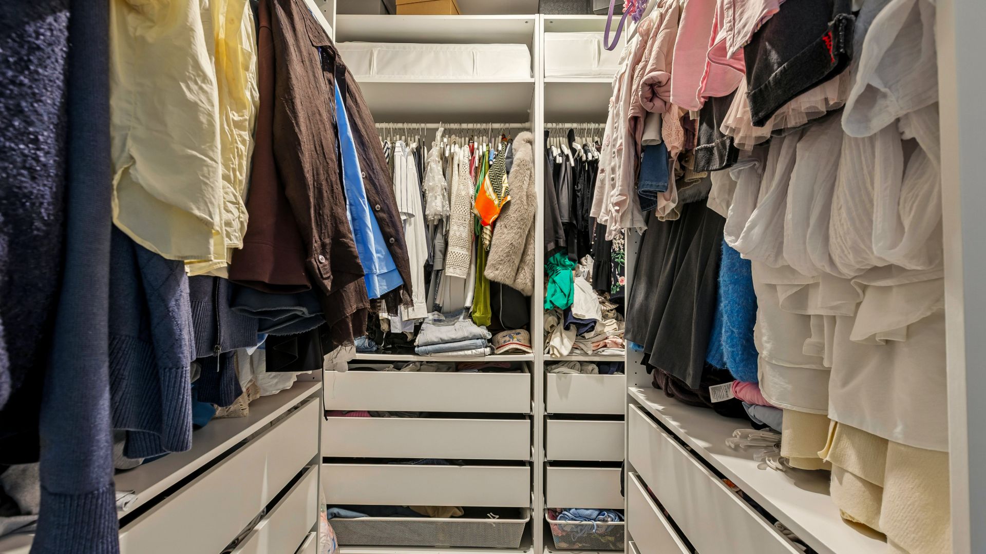Begehbarer Kleiderschrank mit vielen Kleidungsstücken und weißen Schubladen.
