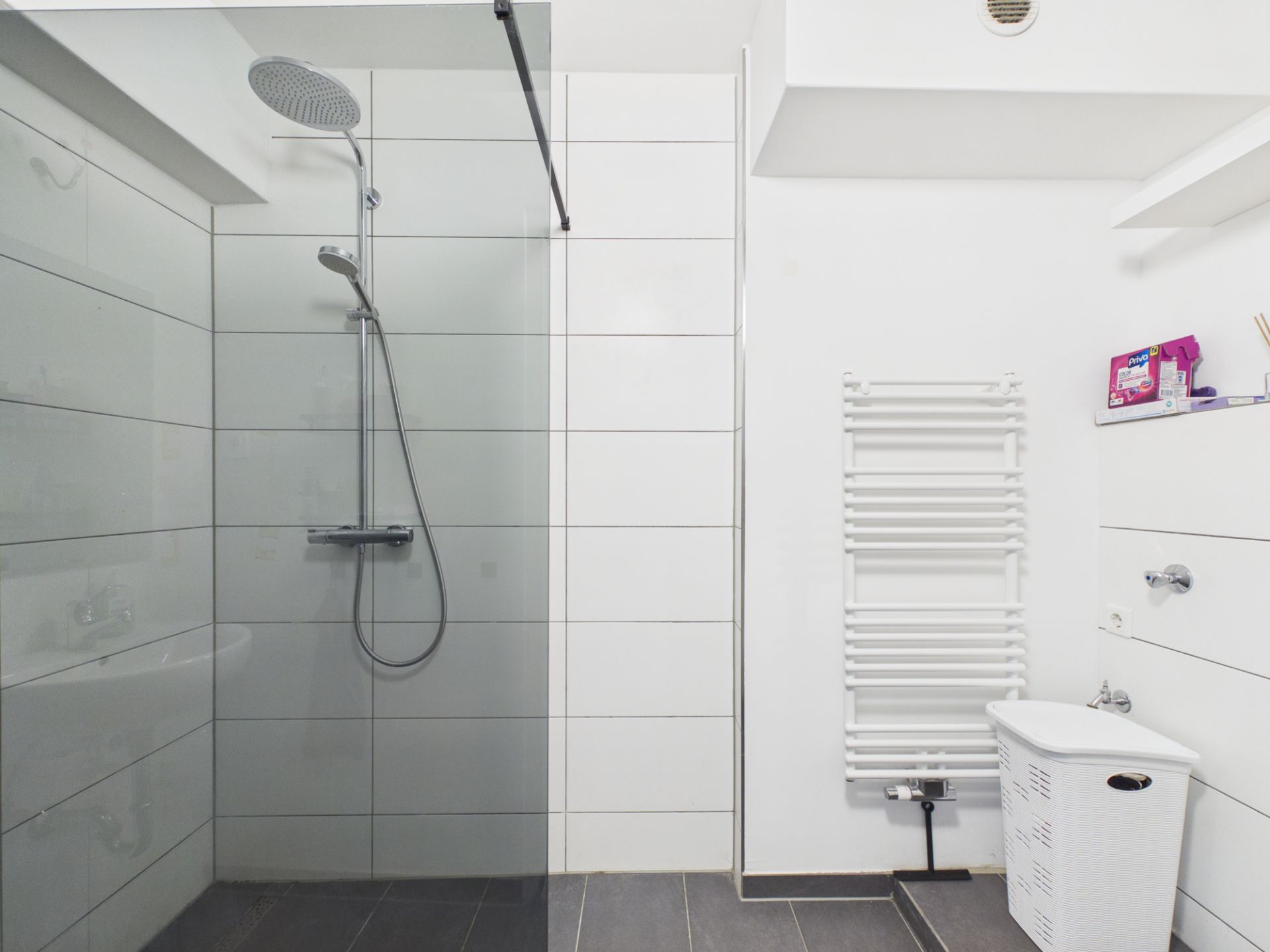 Modernes Bad mit großer Dusche, Handtuchheizkörper und Wäschekorb.