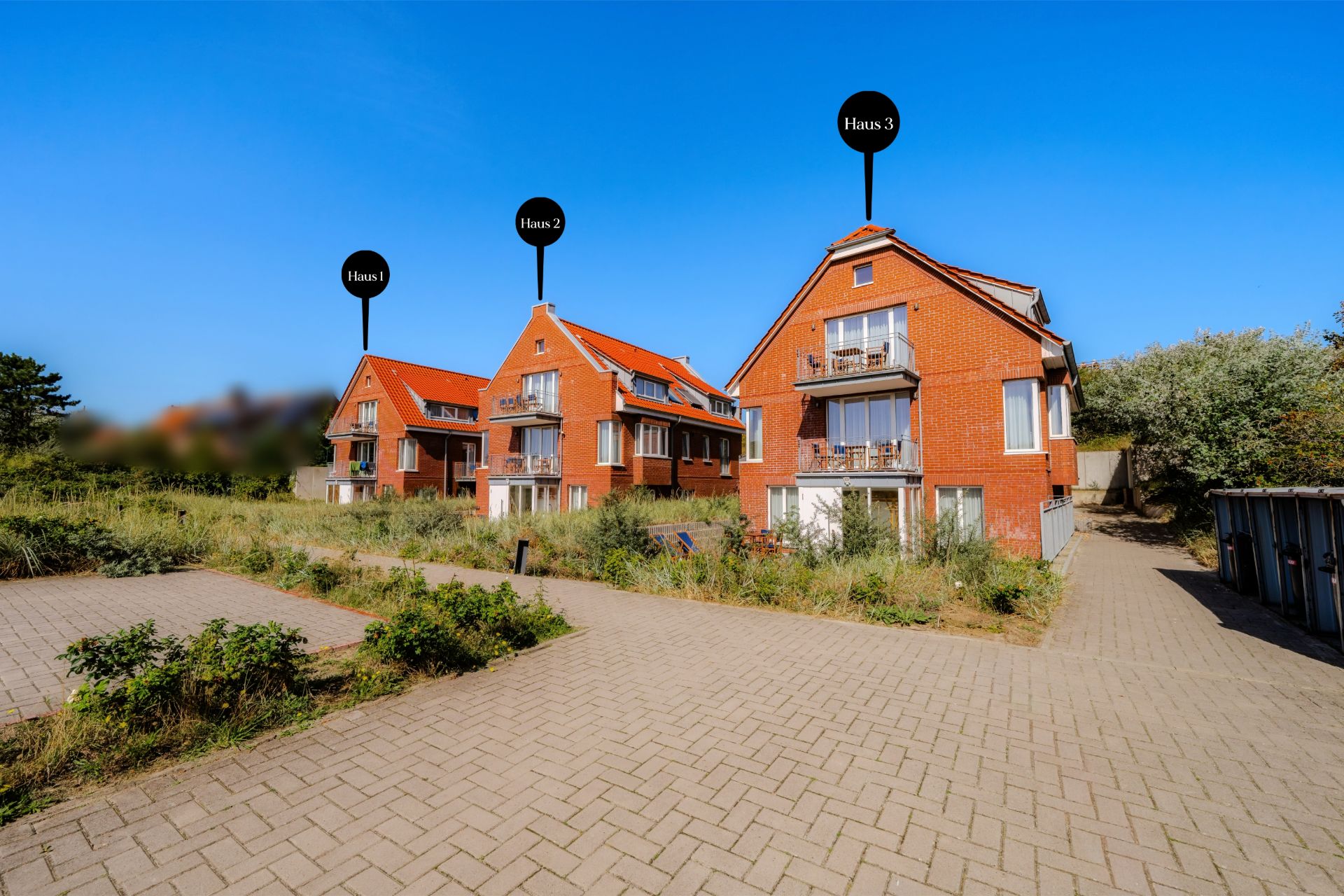 Drei rote Backsteinhäuser mit Balkonen und Gehwegen, umgeben von Grünflächen.