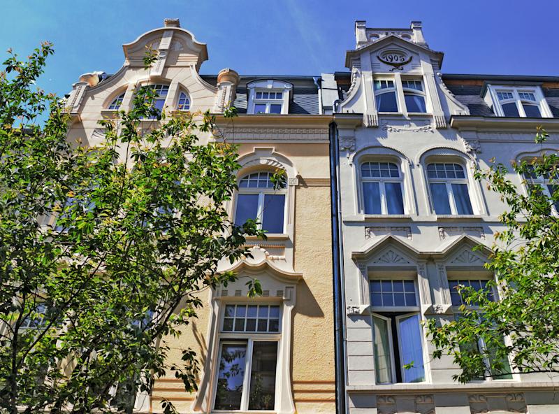 Gepflasterter Platz mit Bäumen, Bänken und Wohngebäuden, darunter ein rotes Haus.