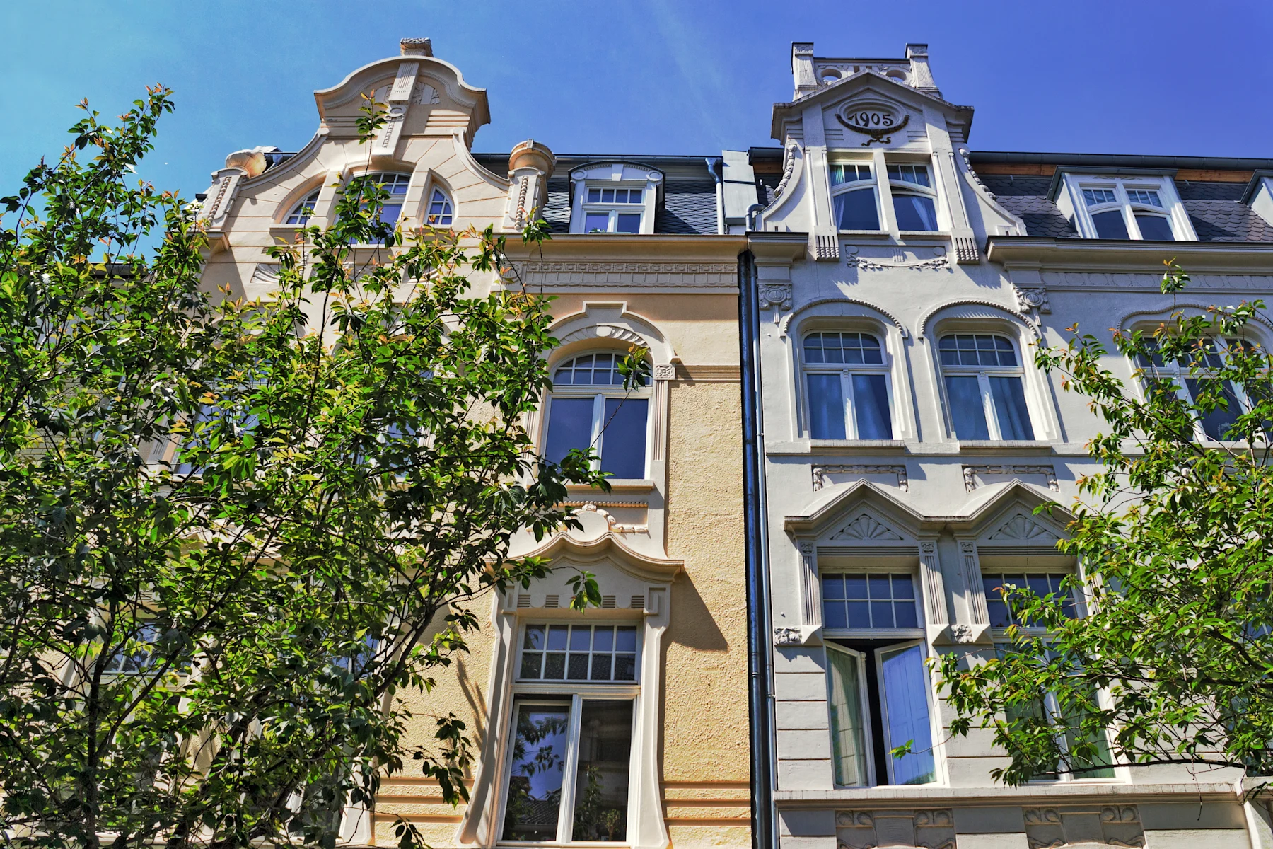 Gepflasterter Platz mit Bäumen, Bänken und Wohngebäuden, darunter ein rotes Haus.
