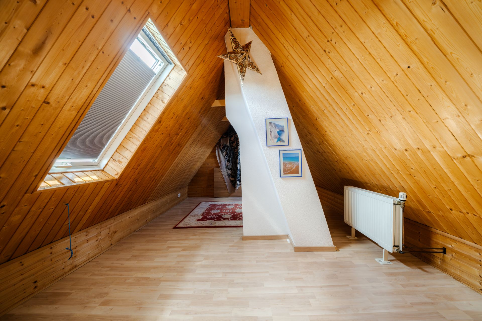 Dachgeschossraum mit Holzverkleidung, Dachfenster, Teppich, Bildern und Heizkörper.