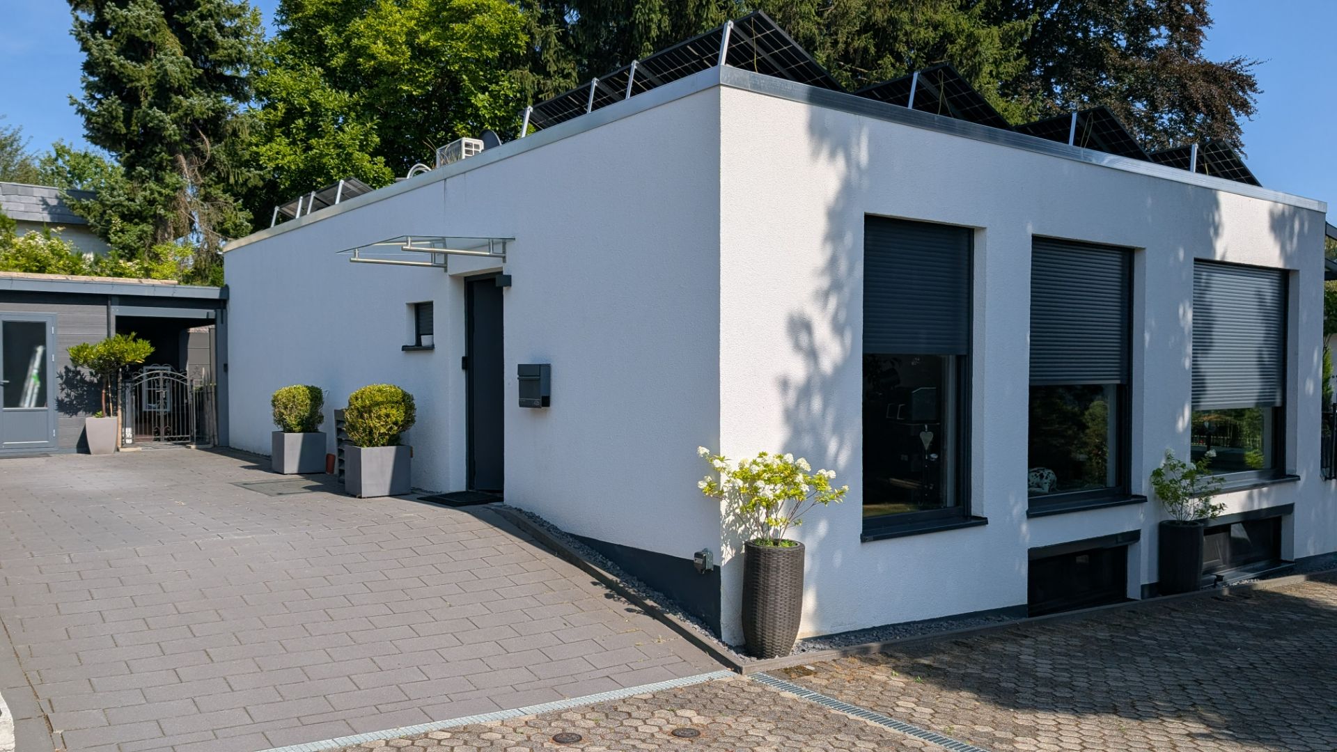 Modernes, weißes Flachbauhaus mit großen Fenstern, Vorgarten und Pflasterauffahrt.