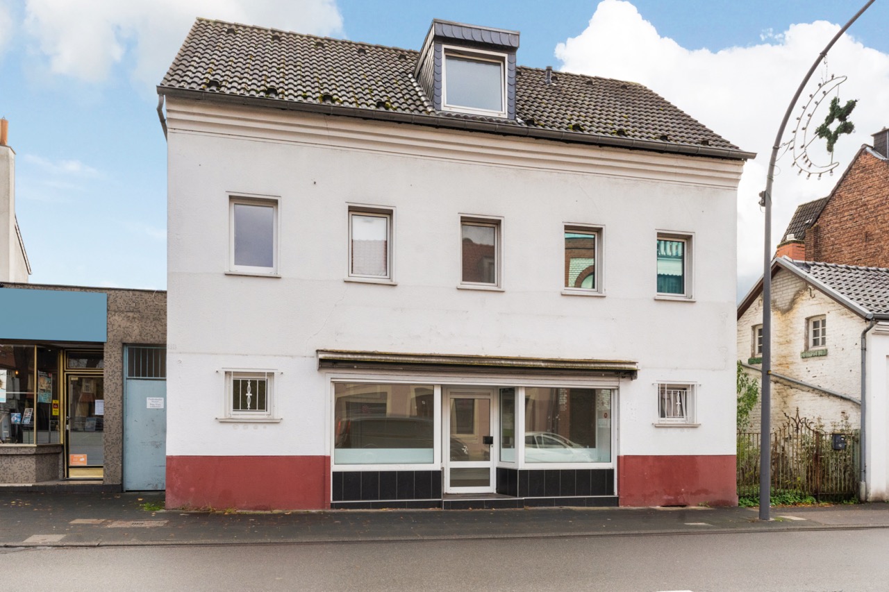 Zweistöckiges Wohnhaus mit Schaufenster und mehreren Fenstern an der Straßenfront.