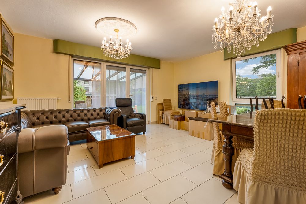 Wohnzimmer mit Ledersofa, Esstisch, Kronleuchtern und bodentiefen Fenstern.