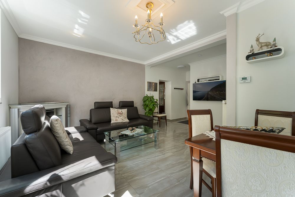 Helles Wohnzimmer mit dunklen Sofas, Glastisch, Esstisch und Wanddekorationen.