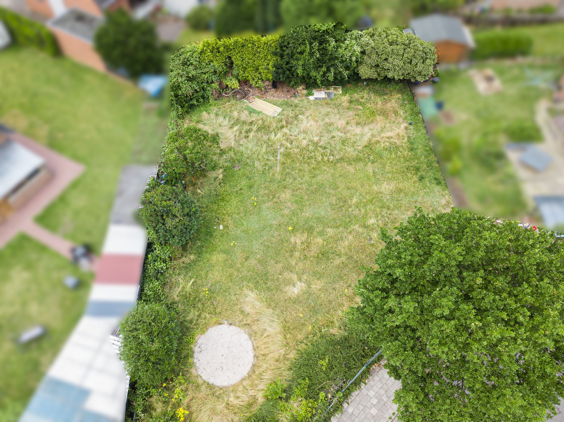 Luftaufnahme eines Gartens mit Rasen, Büschen, Bäumen und einem runden Sandplatz.