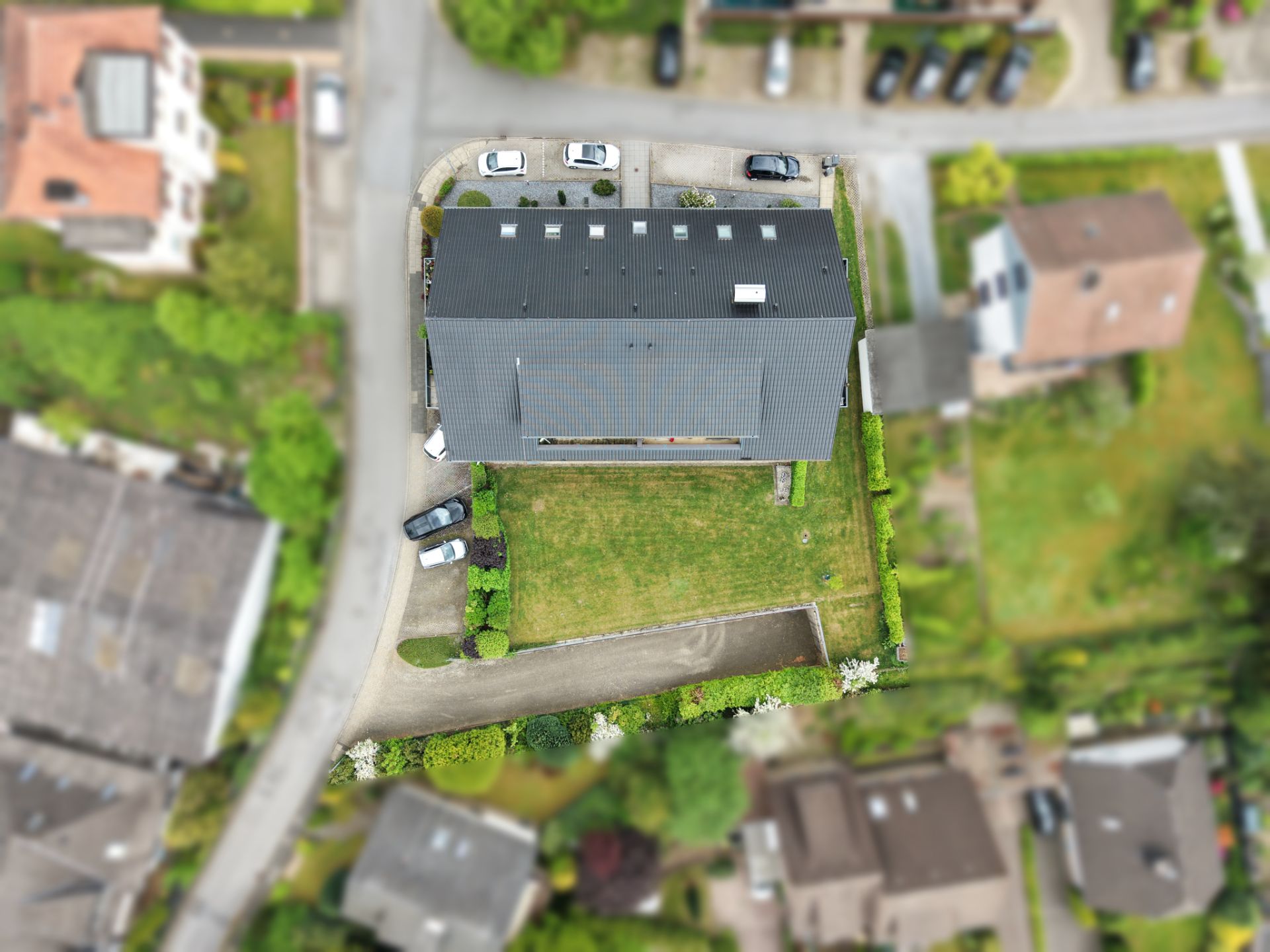 Luftaufnahme eines Hauses mit grauem Dach, großem Garten und Einfahrt in Wohngegend.